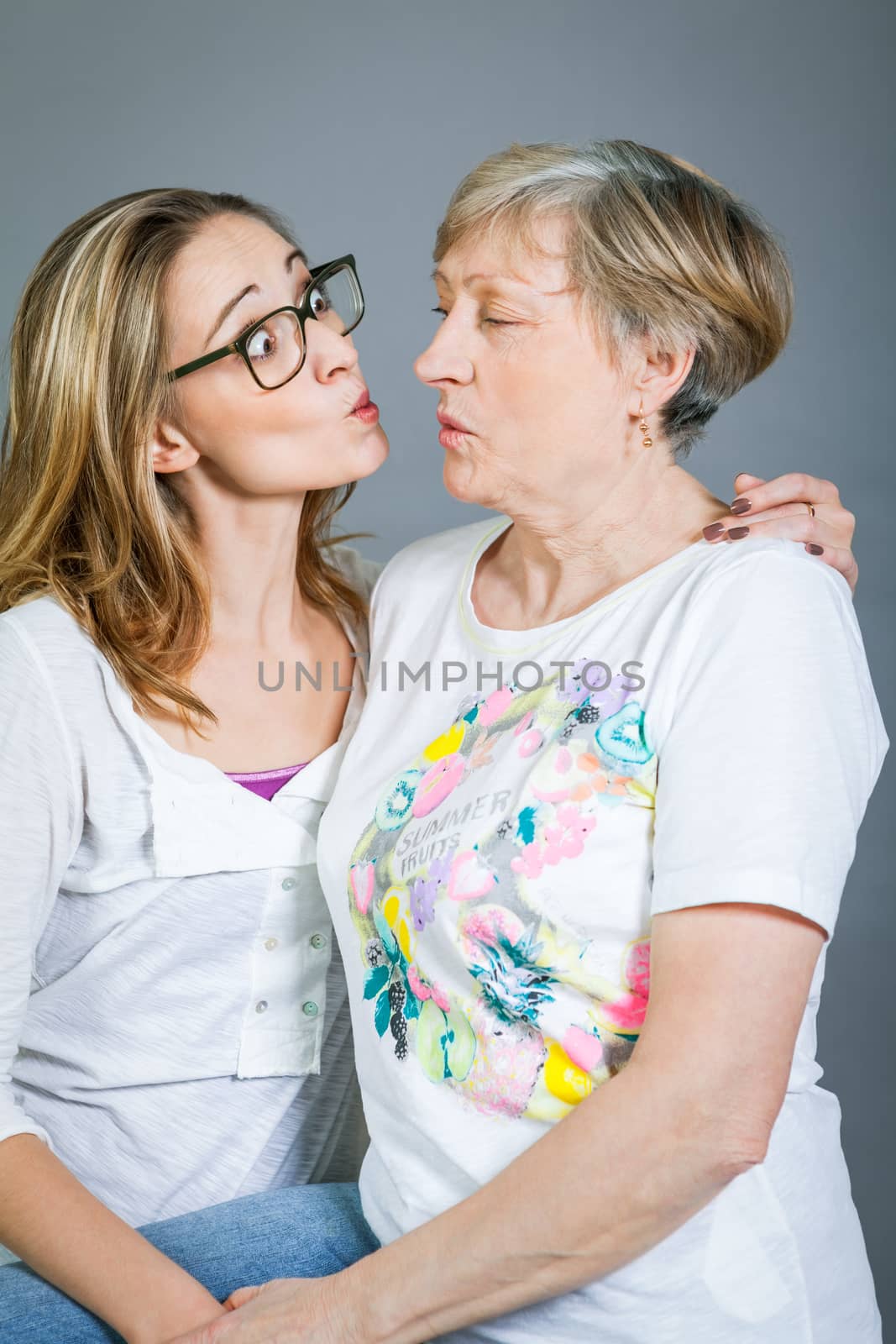 Loving grandmother and teenage granddaughter posing for a portrait holding hands and smiling at the camera, on a grey studio background