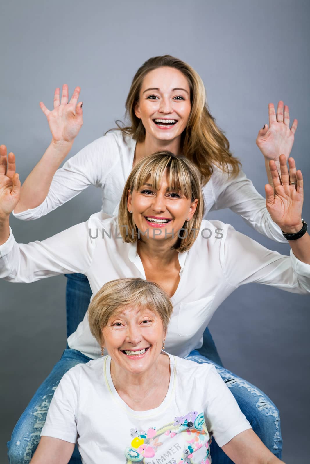 Three generations of attractive women with blond hair and a striking family resemblance posing together arm in arm looking at the camera with friendly smiles