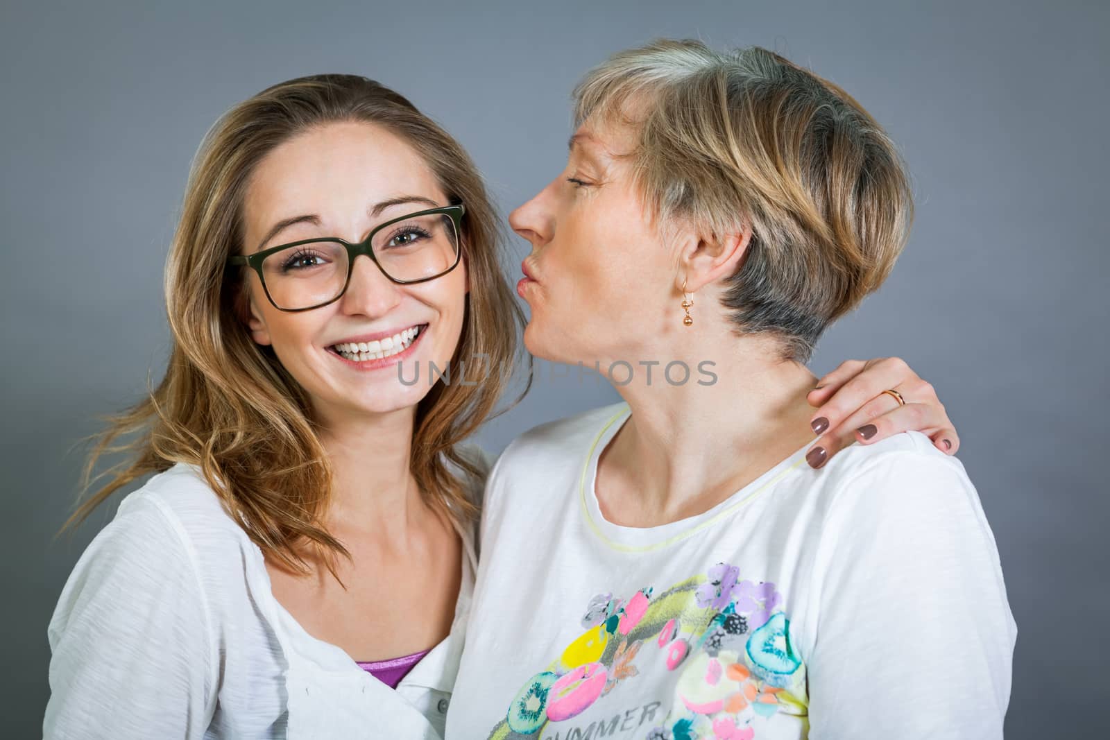 Loving grandmother and teenage granddaughter posing for a portrait holding hands and smiling at the camera, on a grey studio background