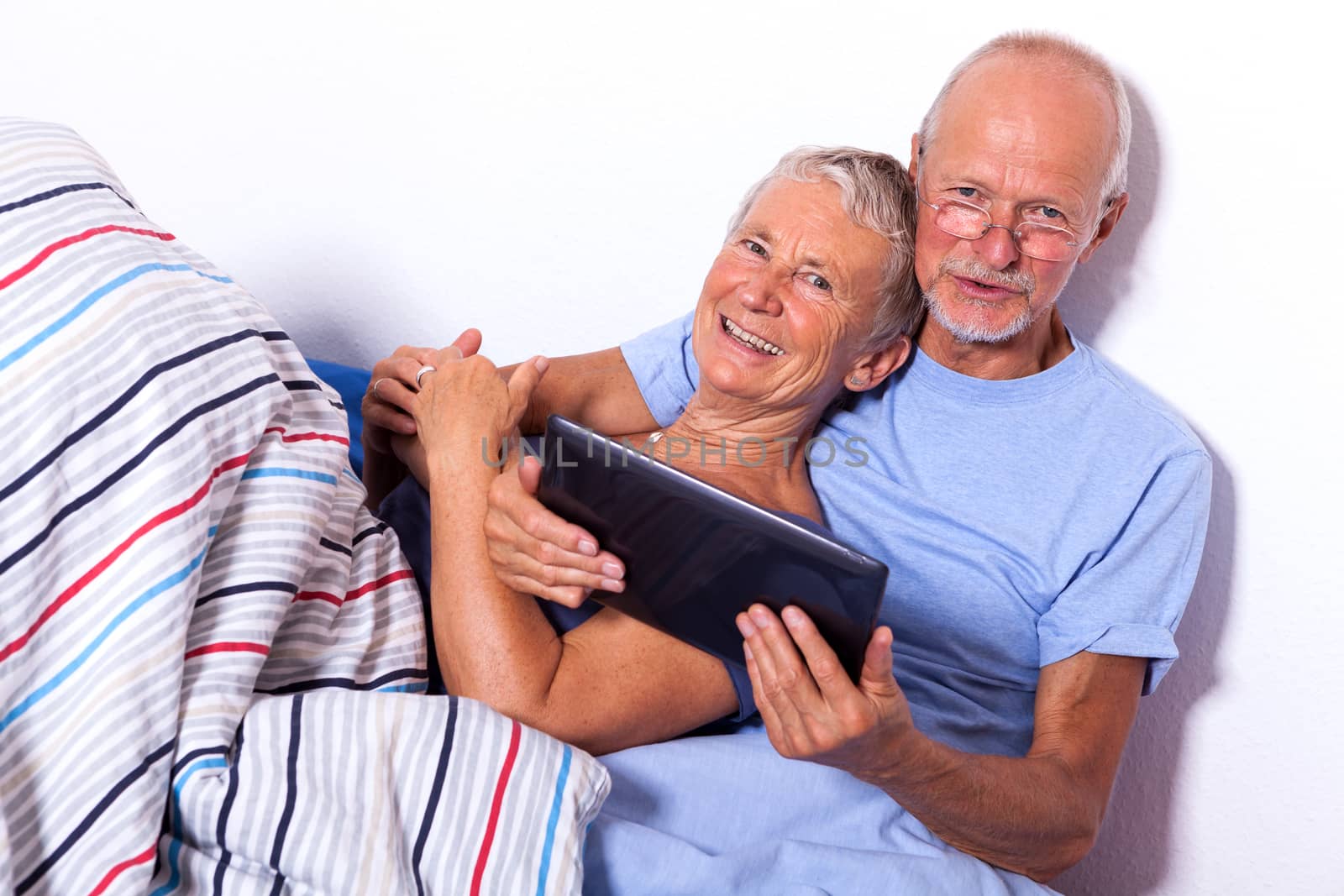 Senior Couple Relaxing in Bed with Tablet Computer and Newspaper