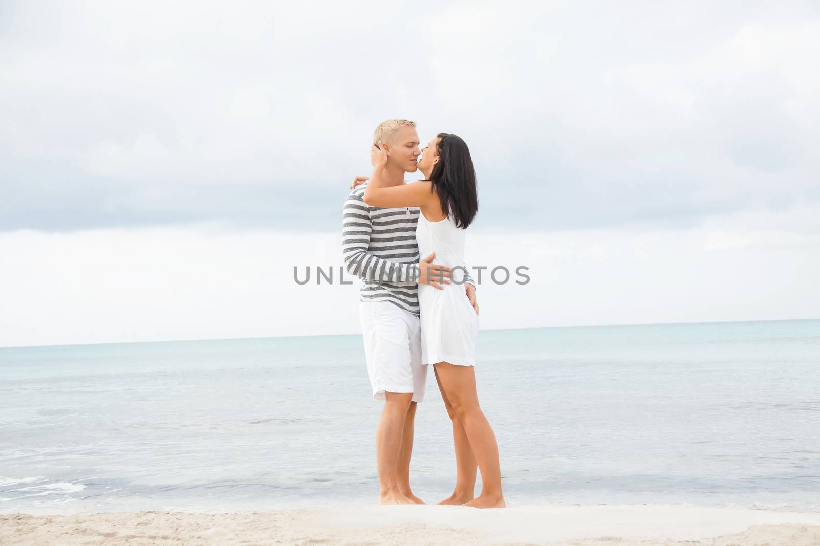 Caucasian happy young couple holding hands while walking barefoot on the beach in a romantic travel destination