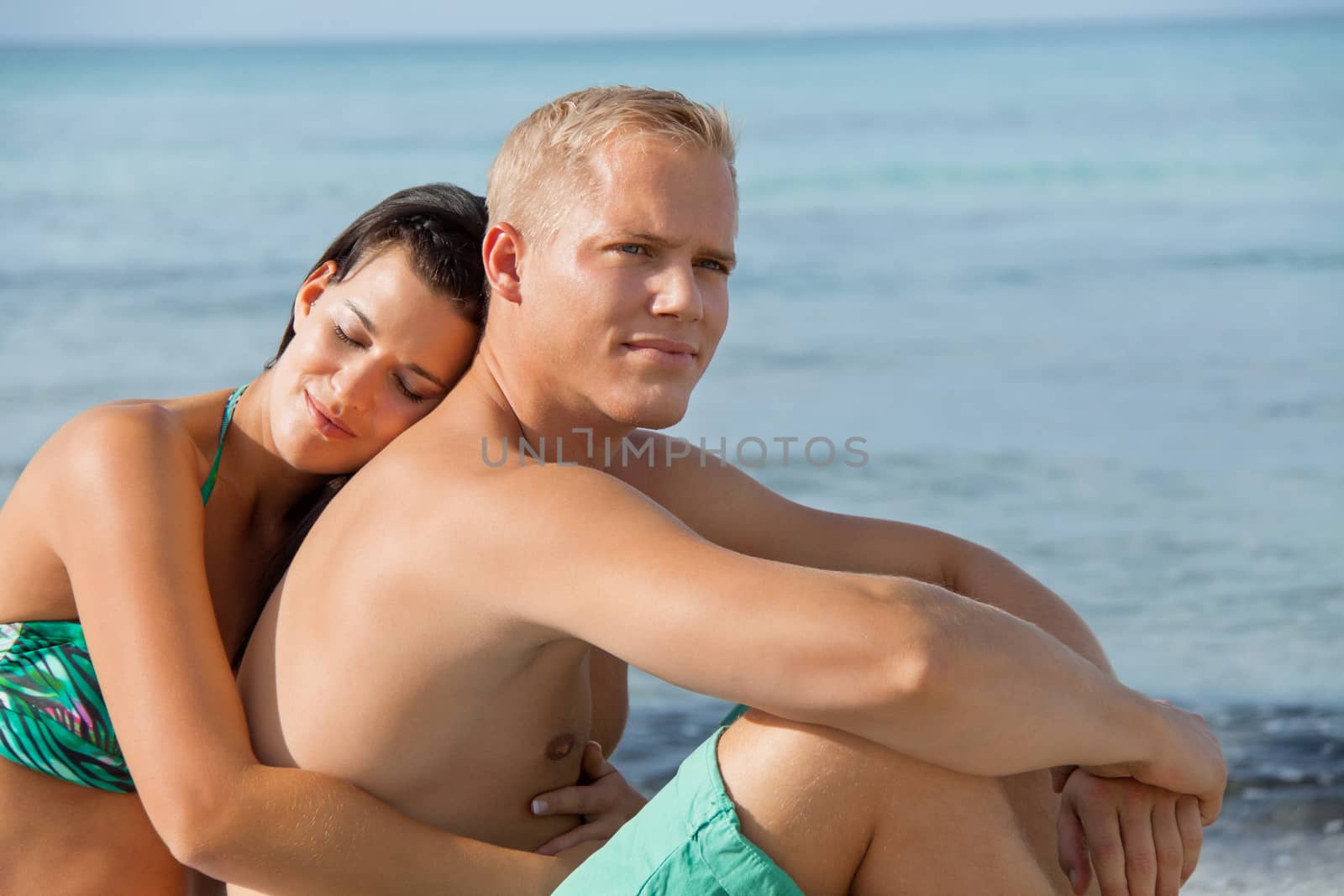 Happy attractive affectionate young couple sunbathing together on the beach in their swimwear while enjoying a tropical summer holiday during the annual vacation