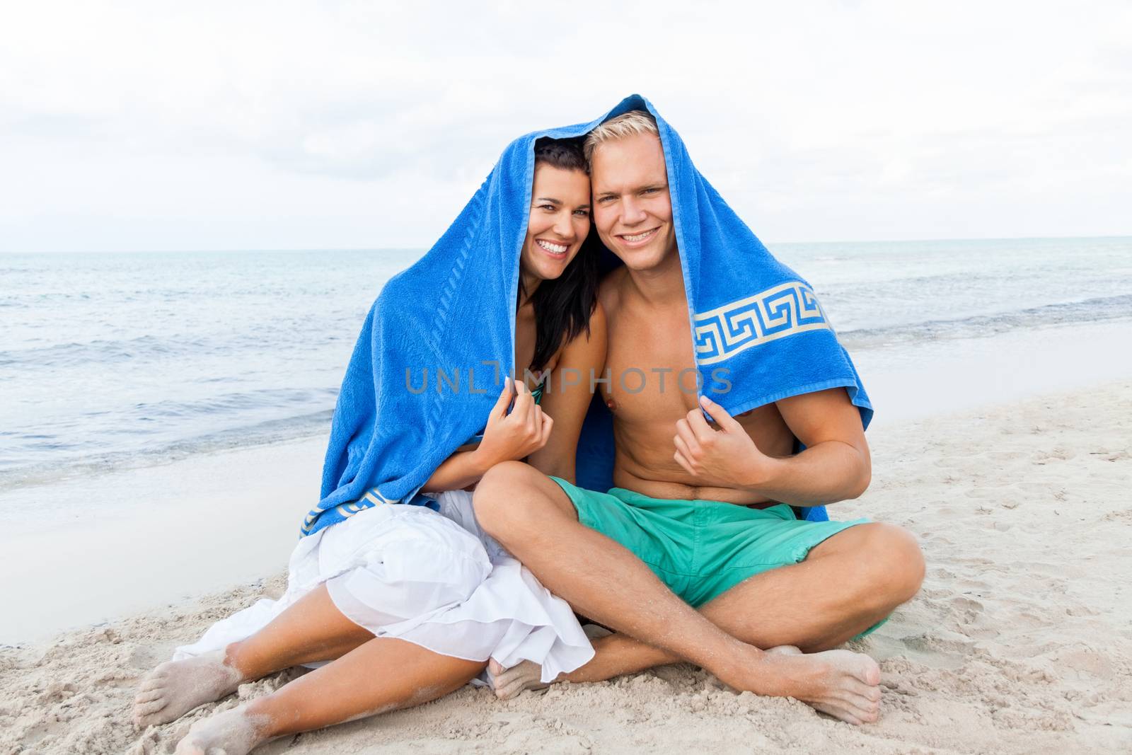 Cheerful Caucasian young happy couple made of a blond handsome man and an attractive brunette woman, with a blue towel covering their heads