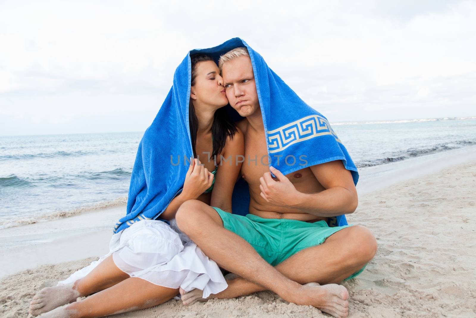 Cheerful Caucasian young happy couple made of a blond handsome man and an attractive brunette woman, with a blue towel covering their heads