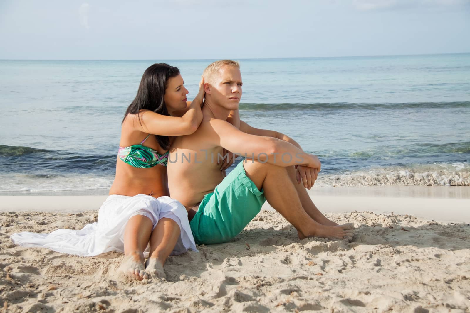 Happy attractive affectionate young couple sunbathing together on the beach in their swimwear while enjoying a tropical summer holiday during the annual vacation