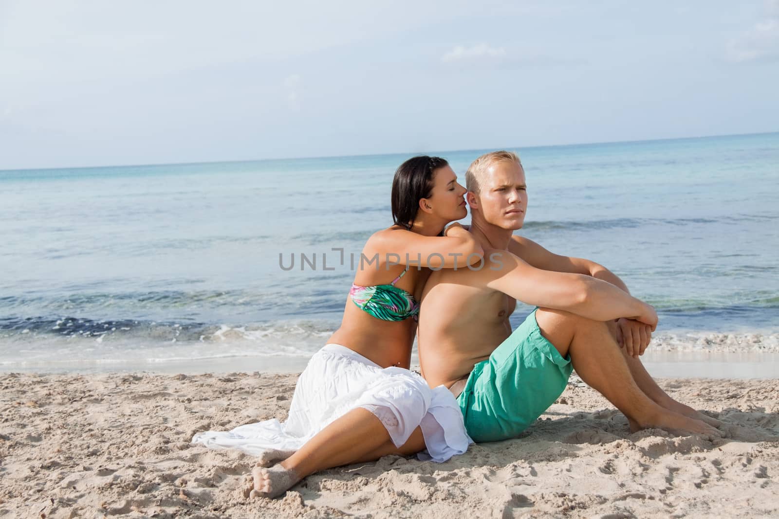 Happy attractive affectionate young couple sunbathing together on the beach in their swimwear while enjoying a tropical summer holiday during the annual vacation