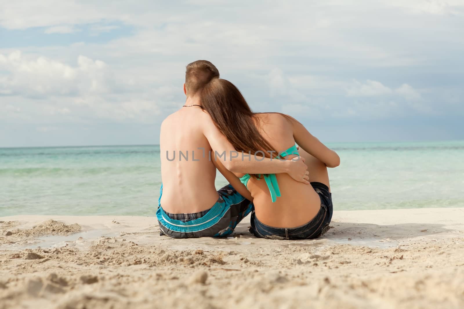 Happy attractive affectionate young couple sunbathing together on the beach in their swimwear while enjoying a tropical summer holiday during the annual vacation