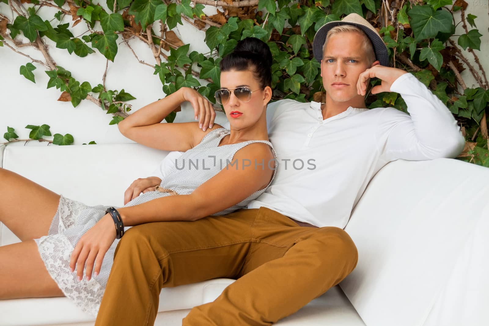 Elegant trendy young couple in fashionable modern clothes and accessories posing outdoors in the summer sunshine in a garden or park