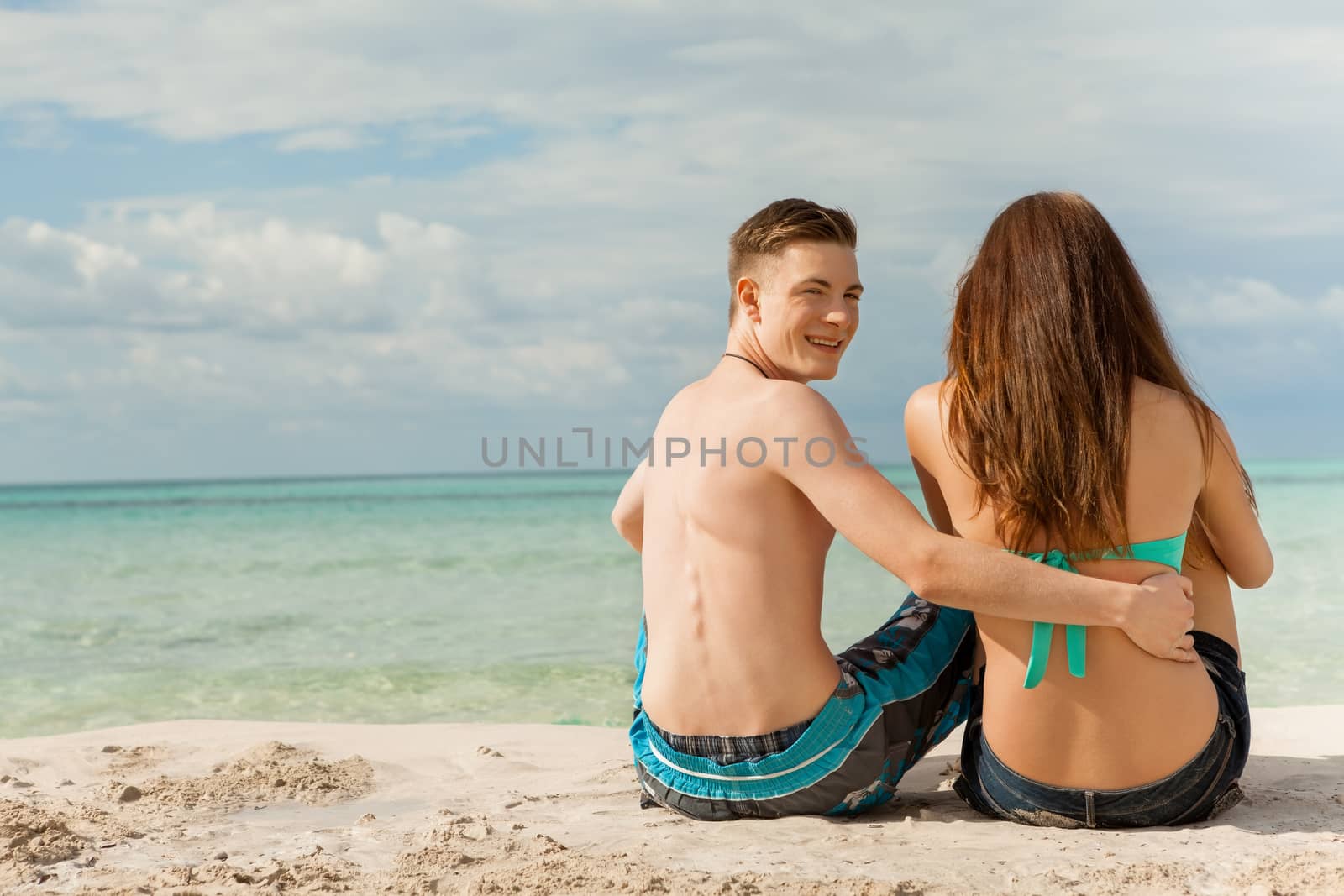 Happy attractive affectionate young couple sunbathing together on the beach in their swimwear while enjoying a tropical summer holiday during the annual vacation