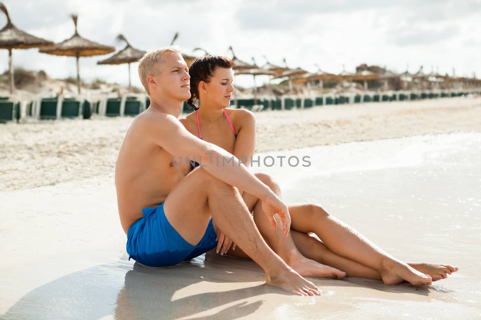 Happy attractive affectionate young couple sunbathing together on the beach in their swimwear while enjoying a tropical summer holiday during the annual vacation