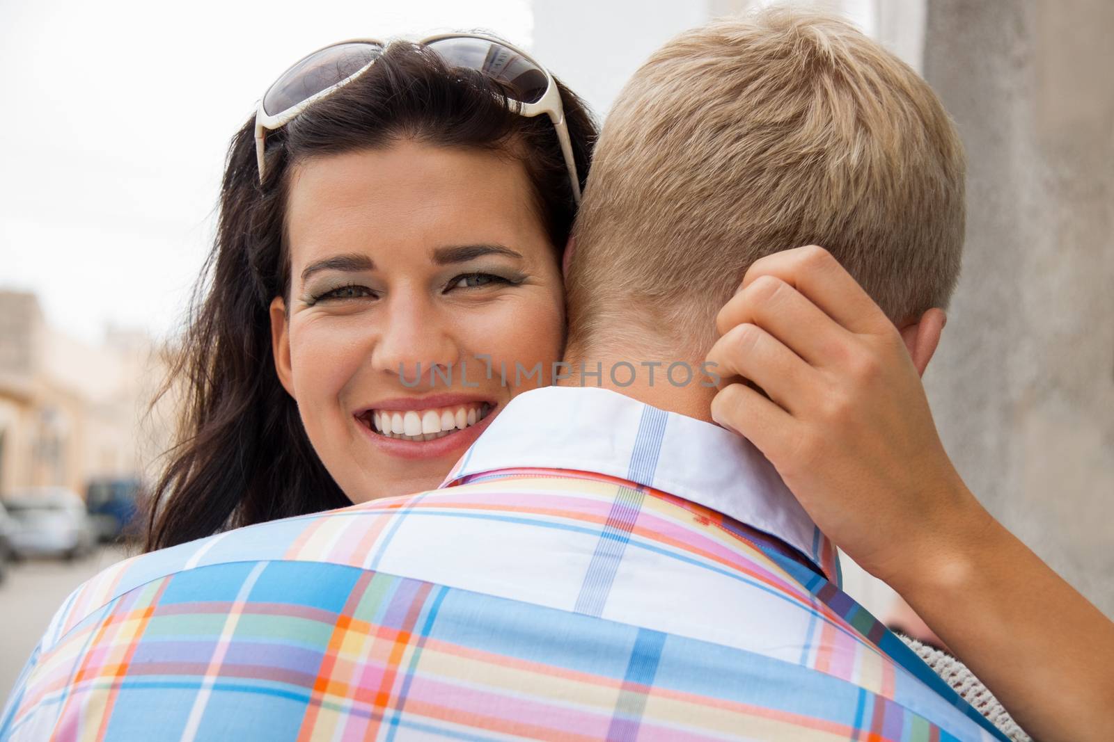 Beautiful radiant young woman beaming with happiness hugging her boyfriend showing her love , focus to her face over his shoulder