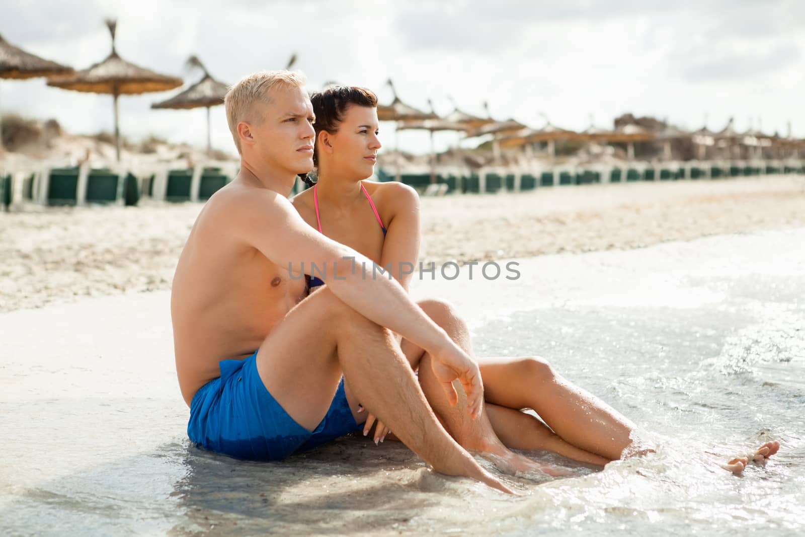 Happy attractive affectionate young couple sunbathing together on the beach in their swimwear while enjoying a tropical summer holiday during the annual vacation