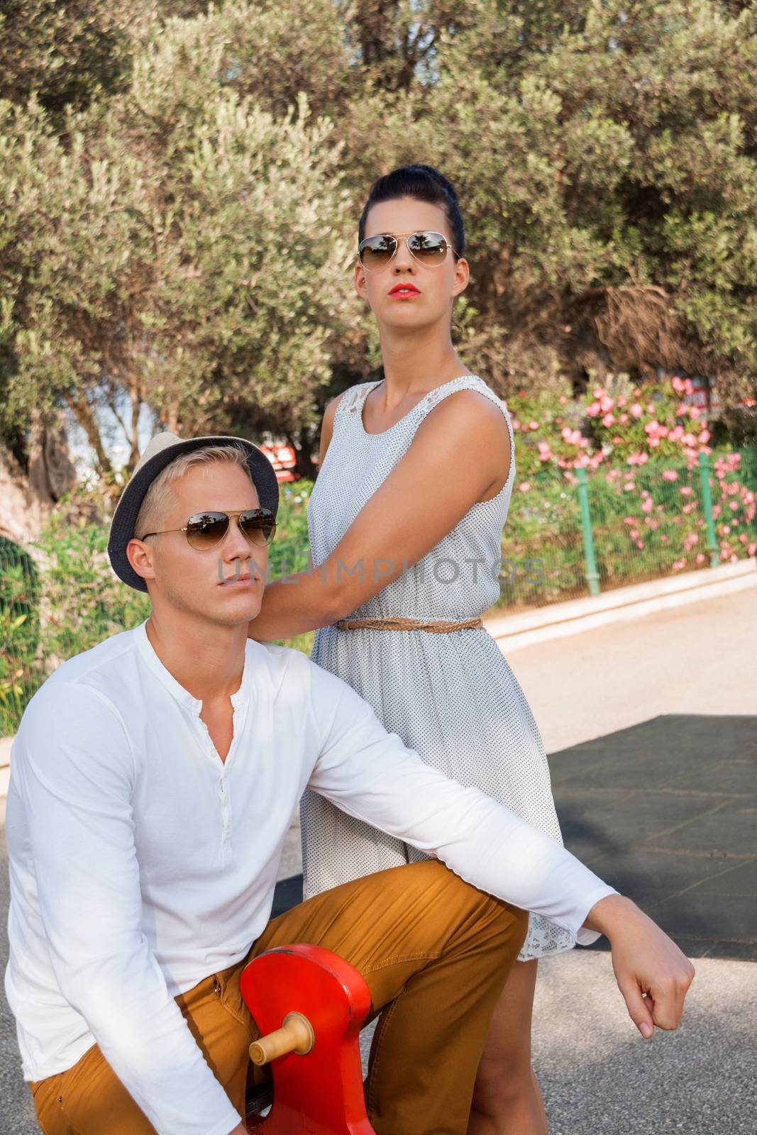 Elegant trendy young couple in fashionable modern clothes and accessories posing outdoors in the summer sunshine in a garden or park