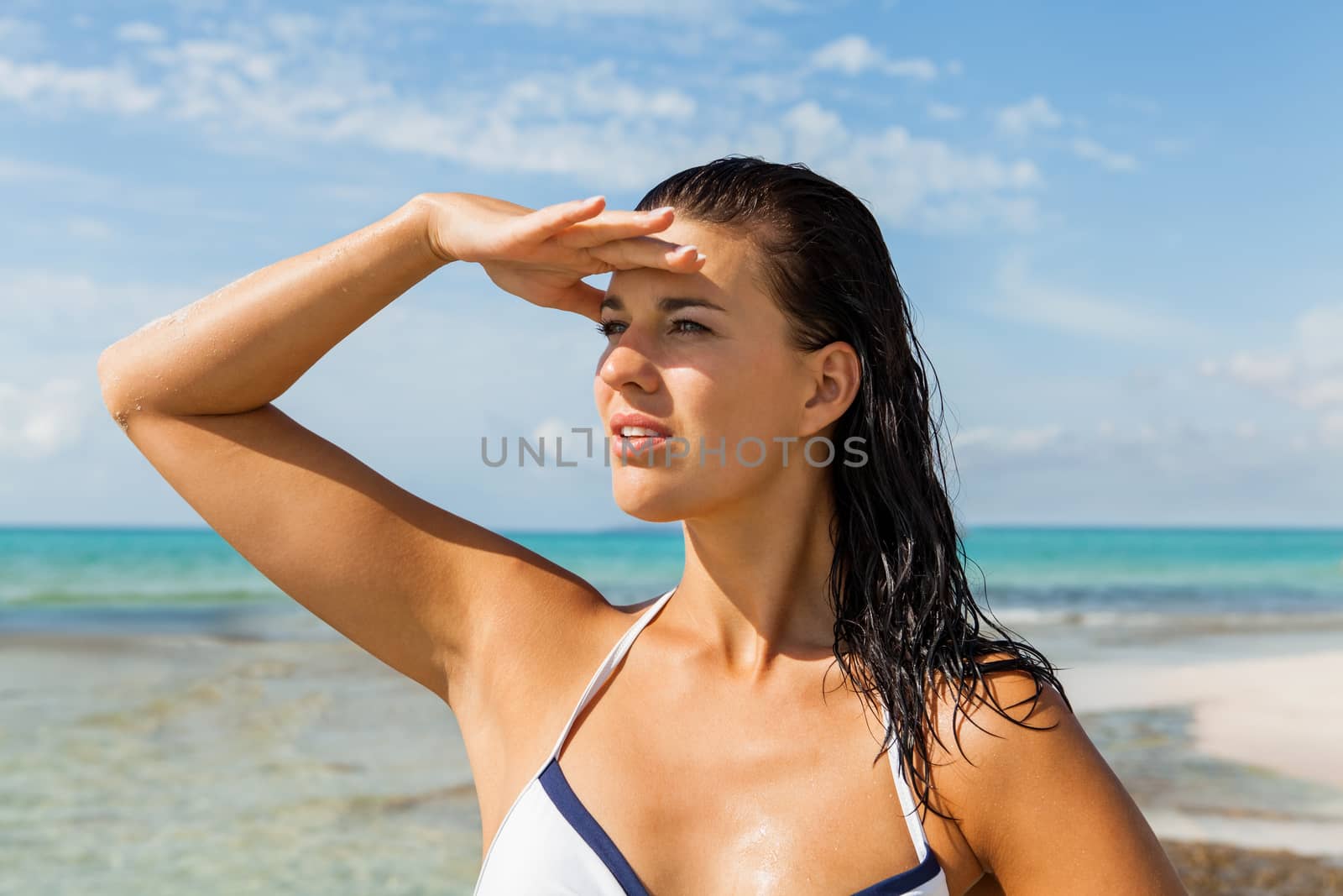 Young woman smiling looking far away shading her eyes with her hand in the beach