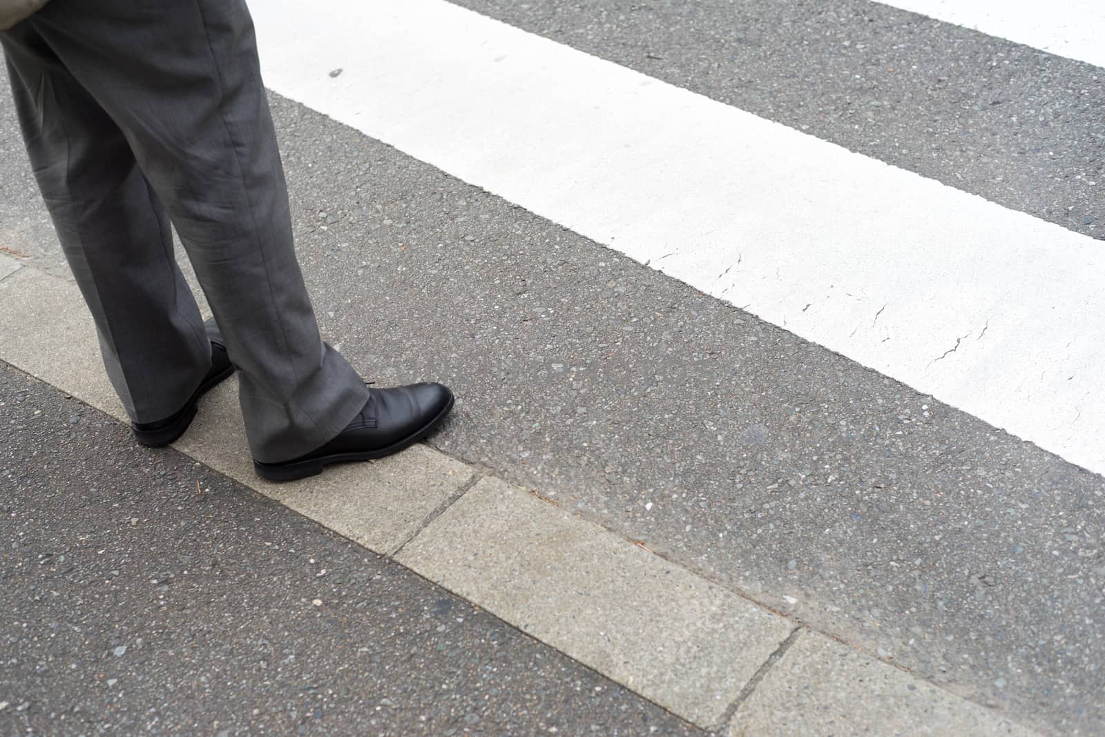 Man legs in slag pants with shoes waiting to cross the street at a crosswalk