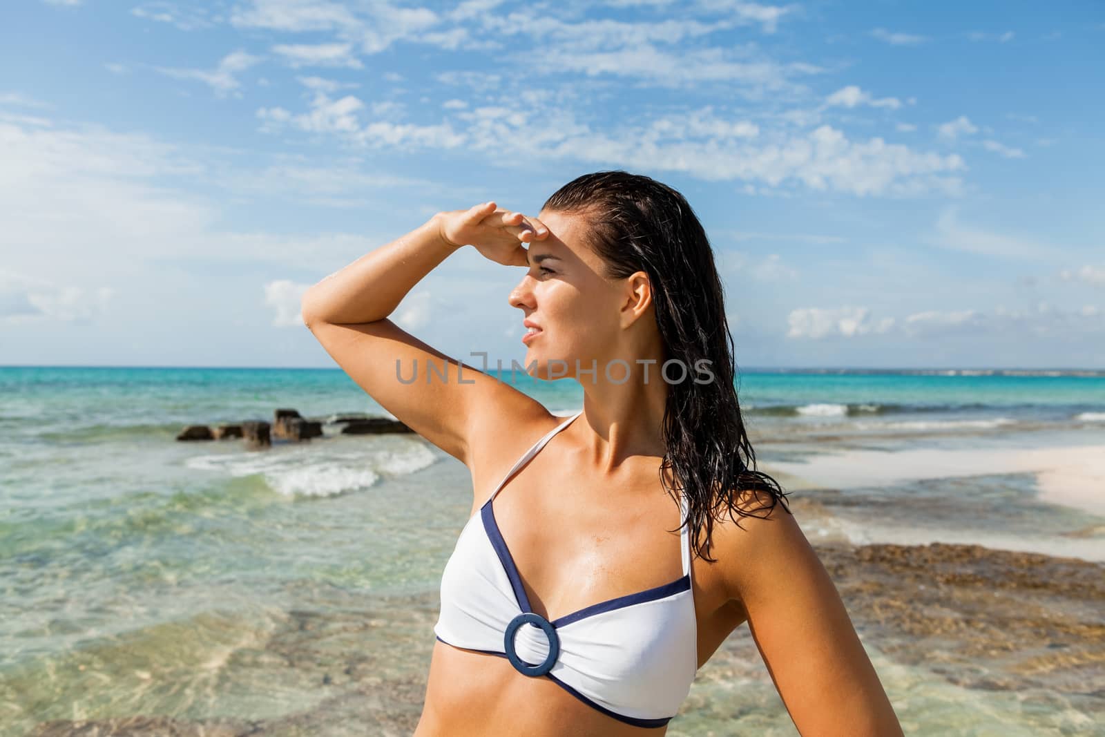 Young woman smiling looking far away shading her eyes with her hand in the beach