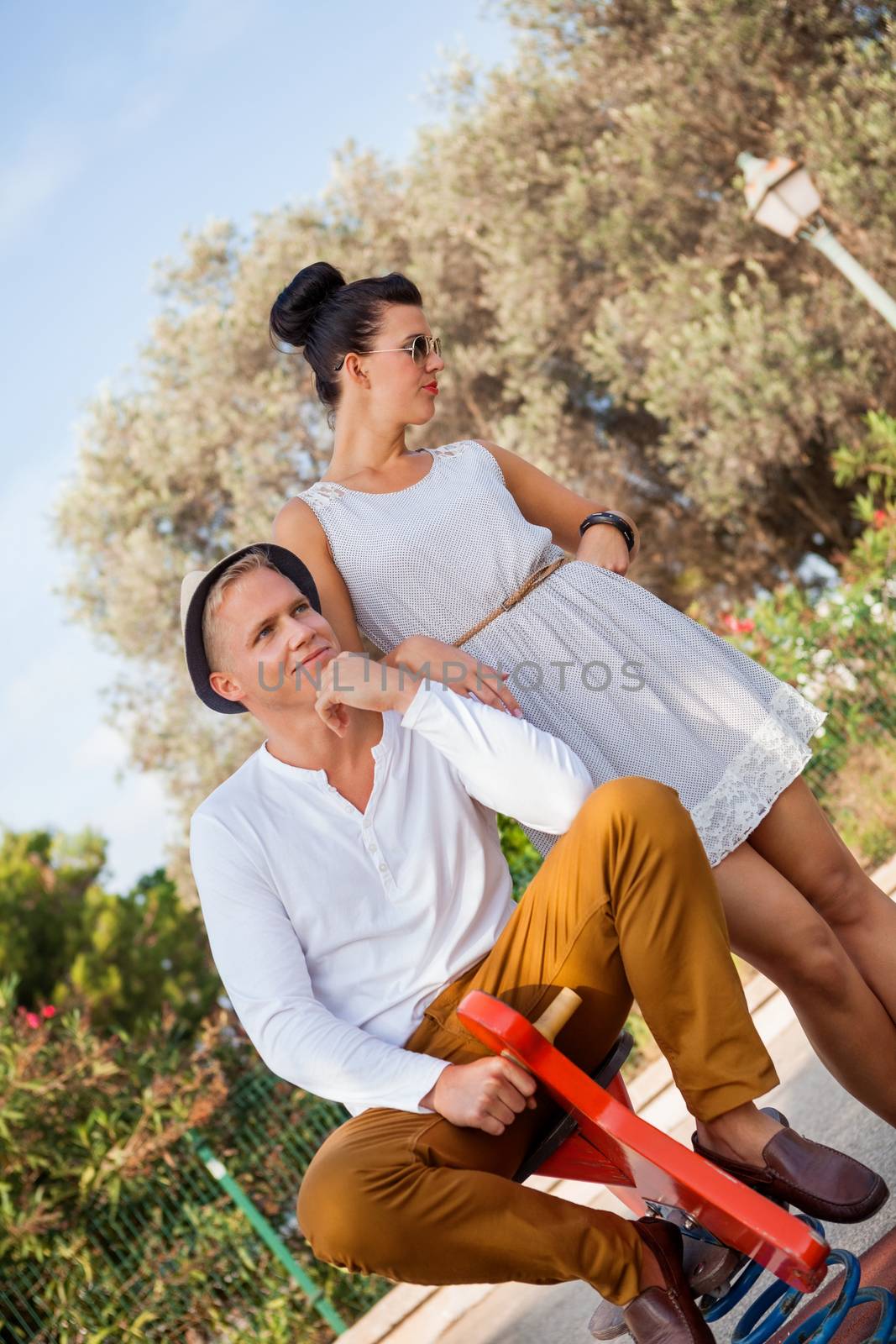 Elegant trendy young couple in fashionable modern clothes and accessories posing outdoors in the summer sunshine in a garden or park