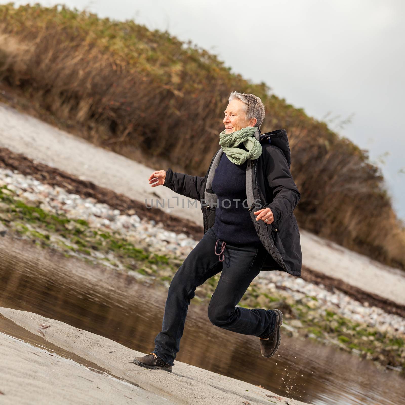 Happy senior woman frolicking on the beach striding along with outspread arms and a smile of appreciation as she enjoys nature and the freedom of her retirement