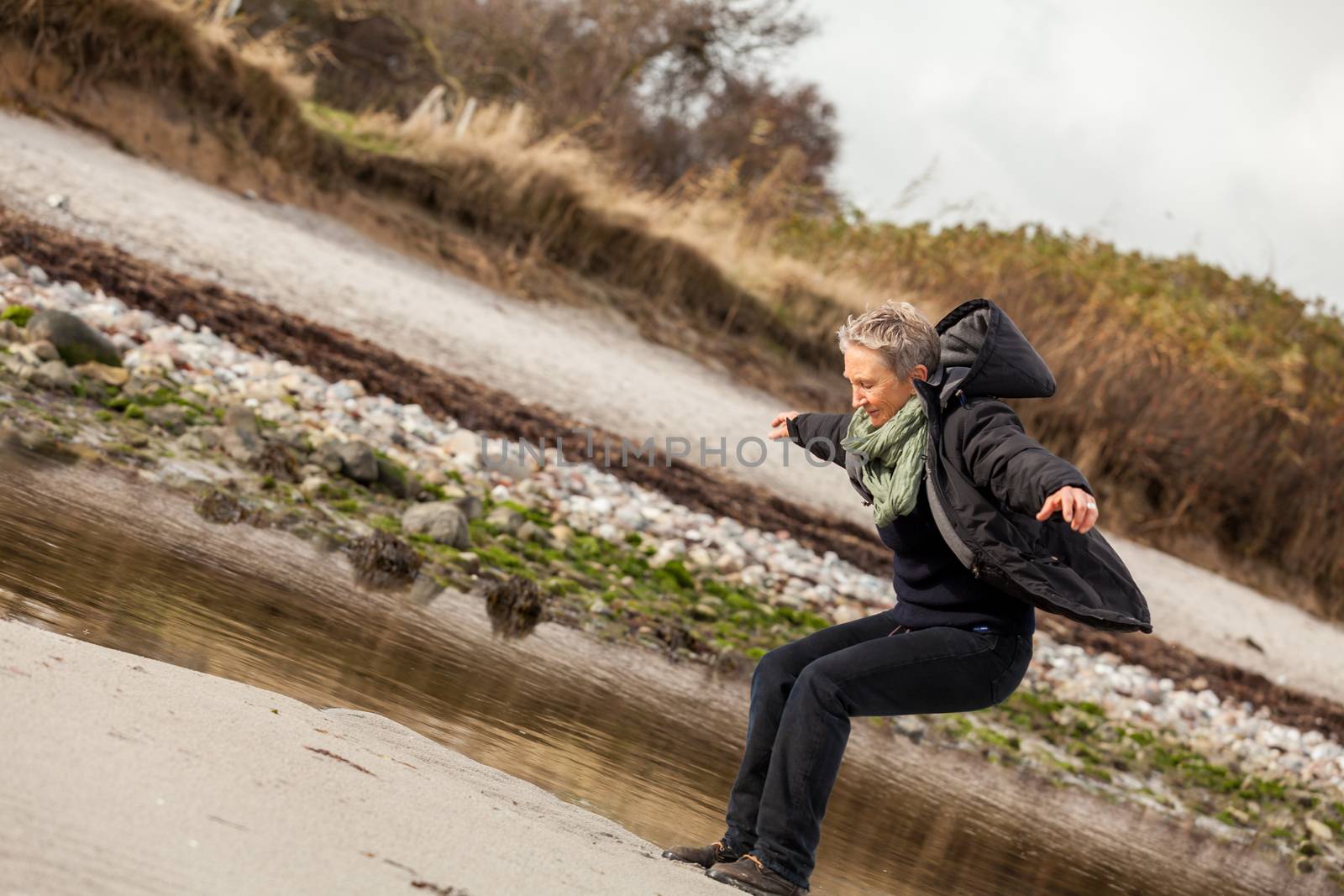 Happy senior woman frolicking on the beach striding along with outspread arms and a smile of appreciation as she enjoys nature and the freedom of her retirement