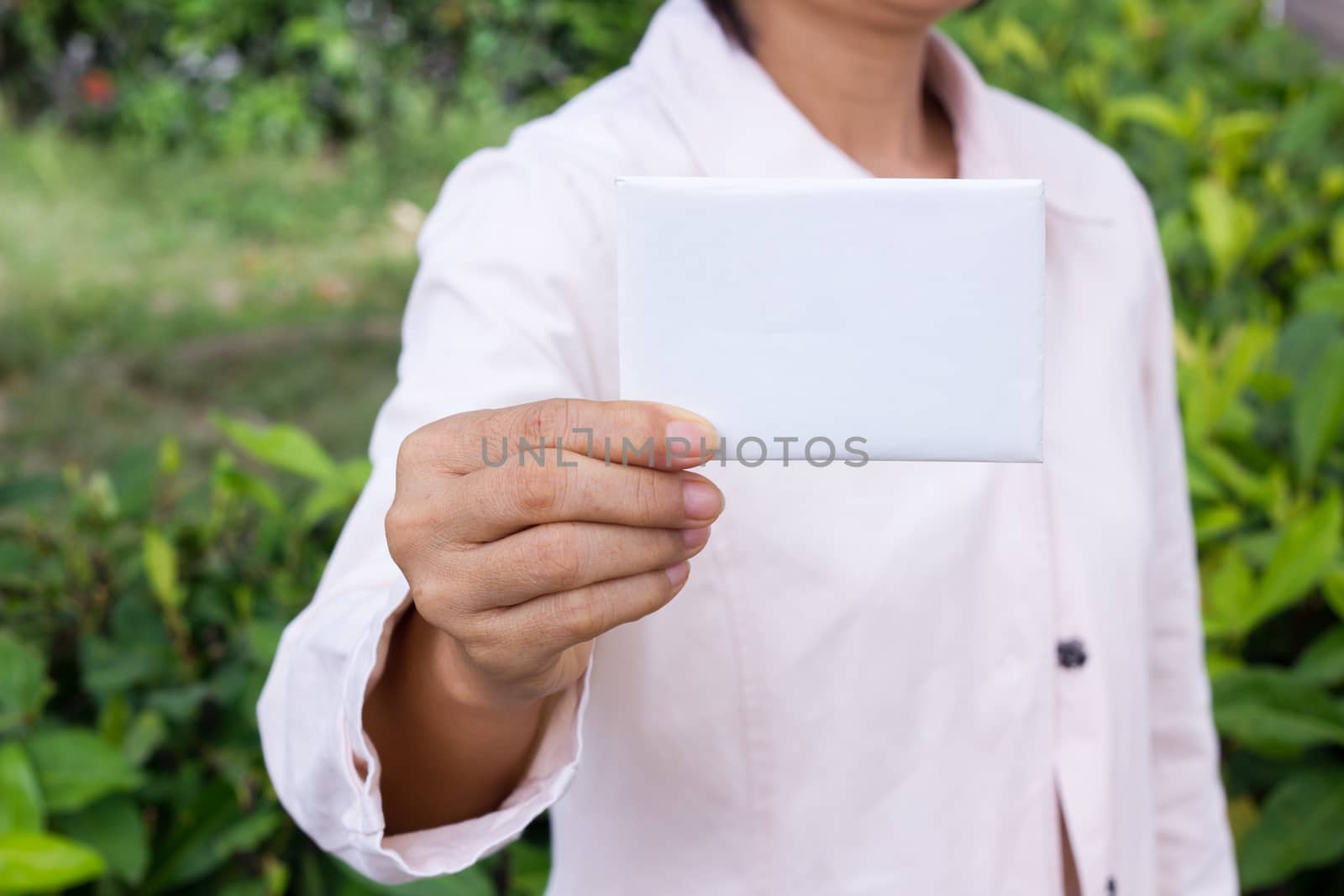 woman's hand showing business card - closeup shot on garden background.