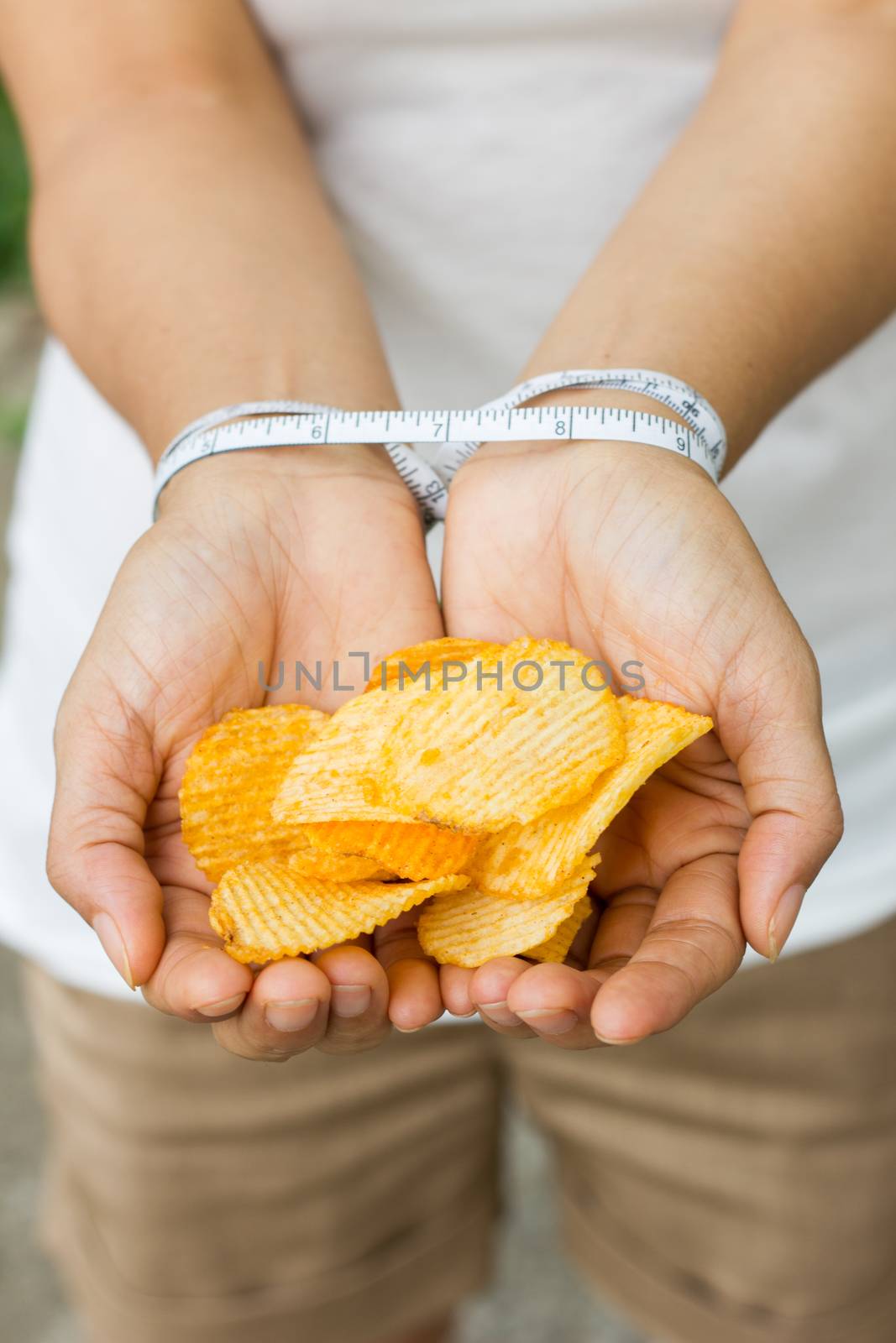Potato chips in woman hand, tied with Measuring tape, concept stopping fat food