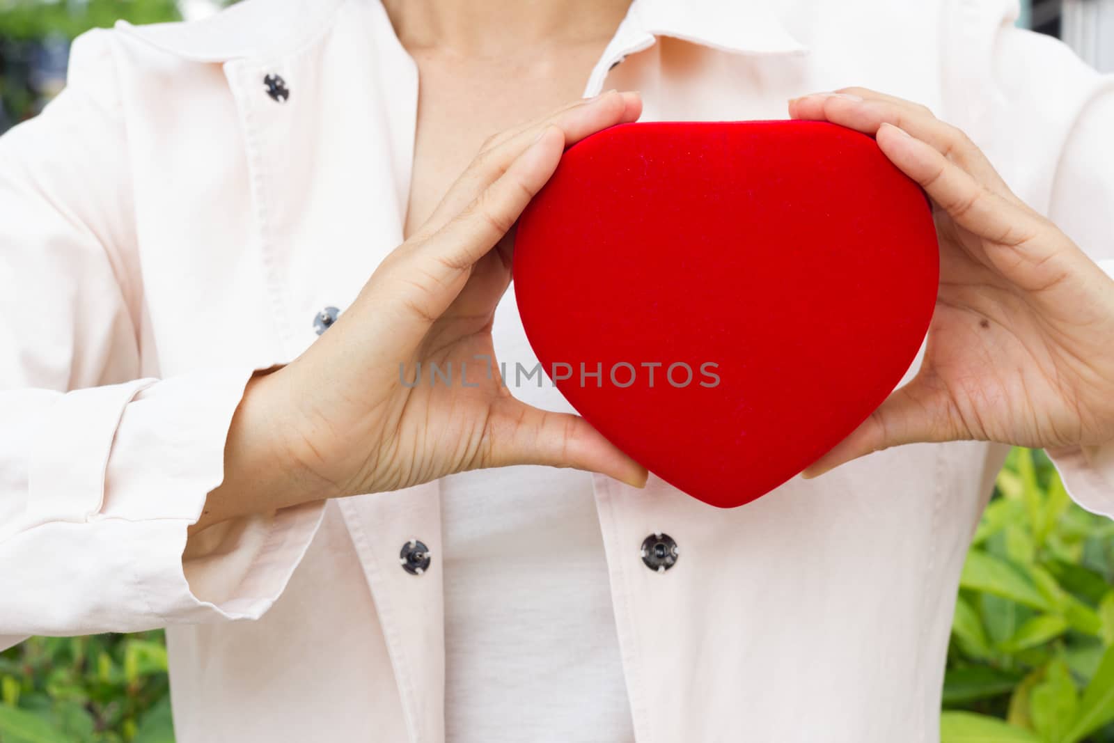 Woman holding heart-shaped red box next to her chest.