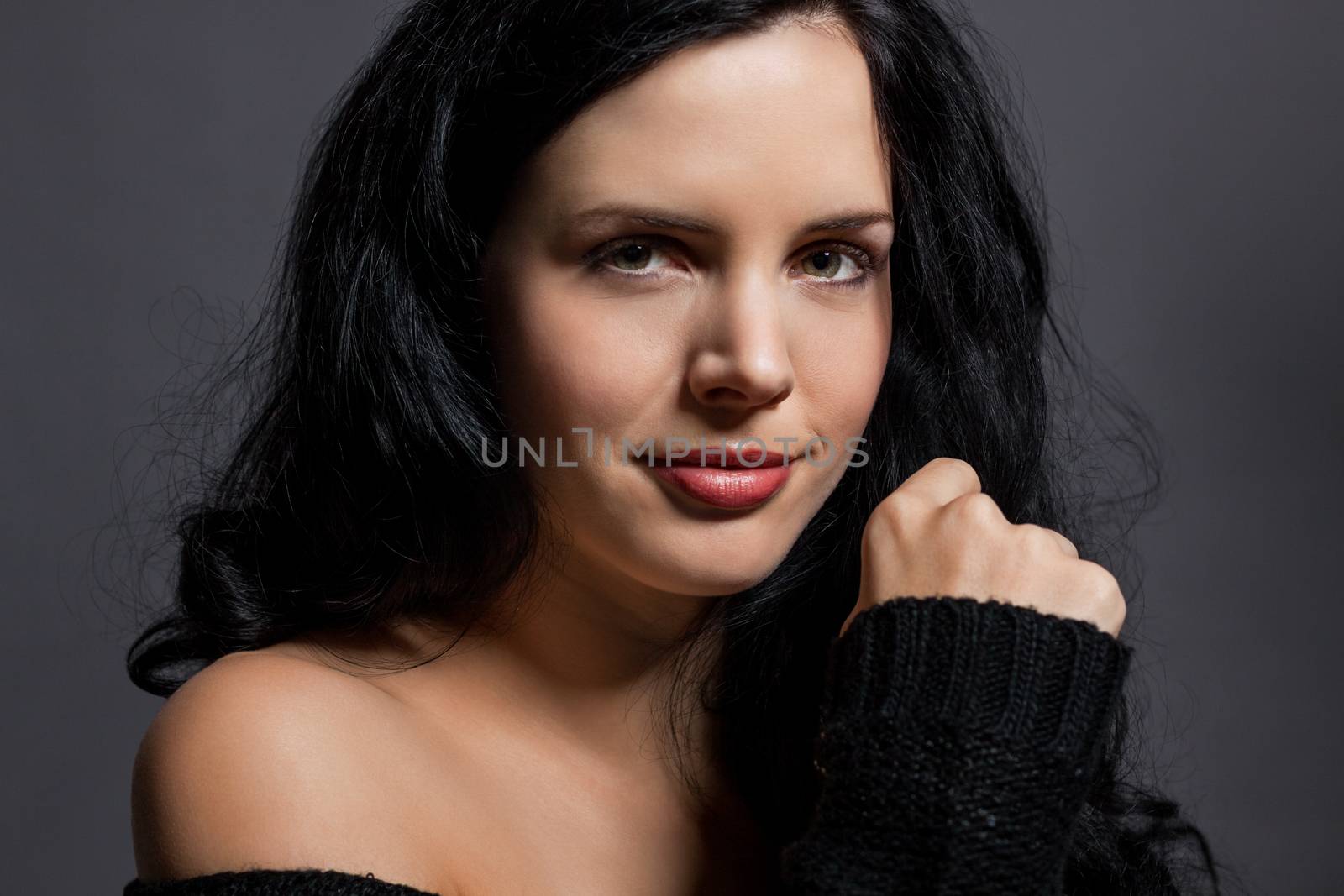 Dark moody portrait of a sultry beautiful woman with long black hair wearing a stylish off the shoulder top , head and shoulders against a grey studio background