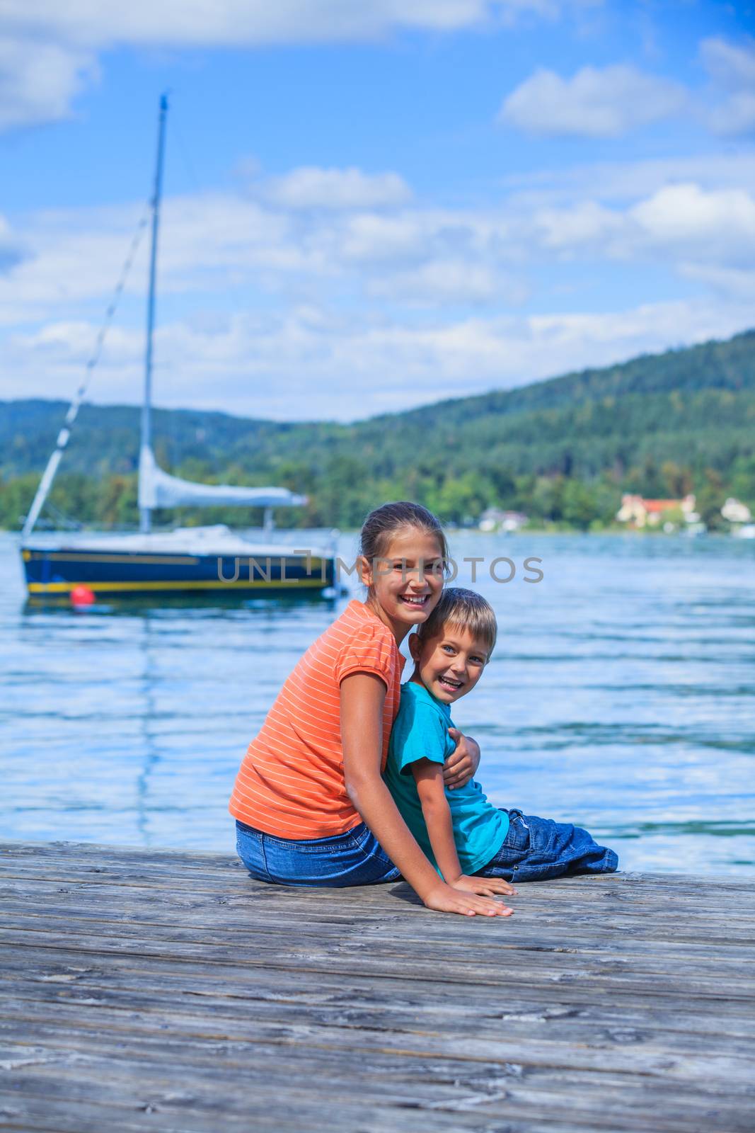 Summer vacation  at the lake - two happy kids resting on the pier and watching on the yacht