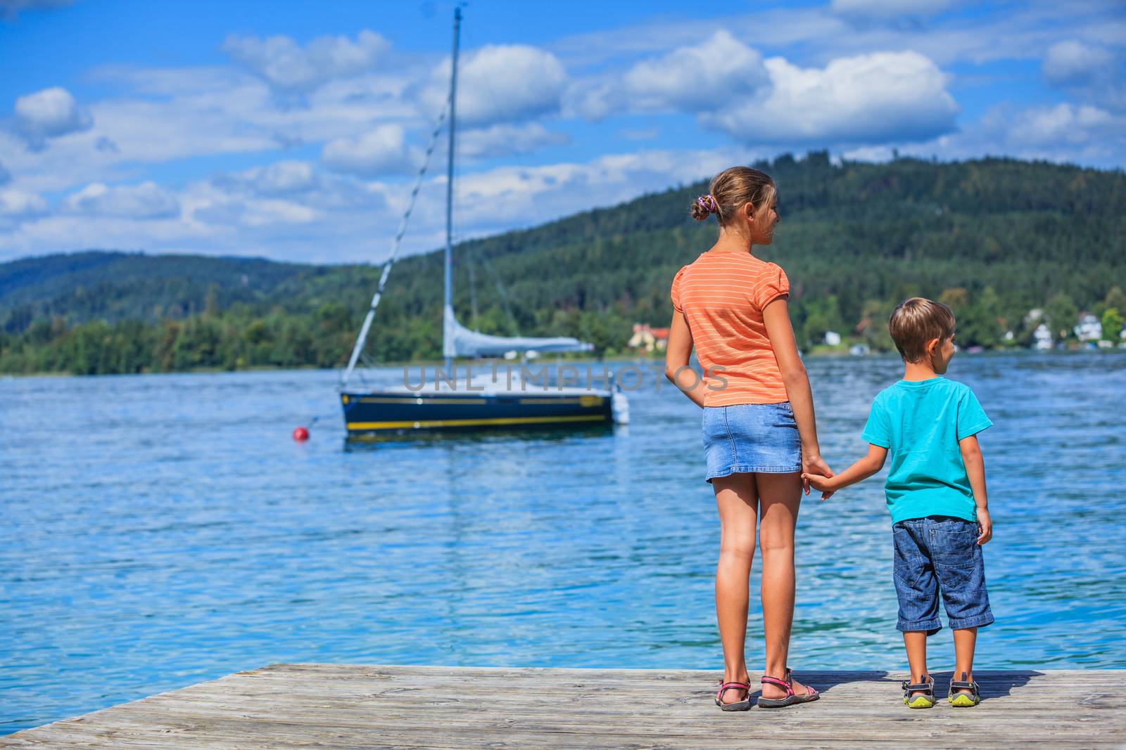 Summer vacation  at the lake - two happy kids walking on the pier and watching on the yacht