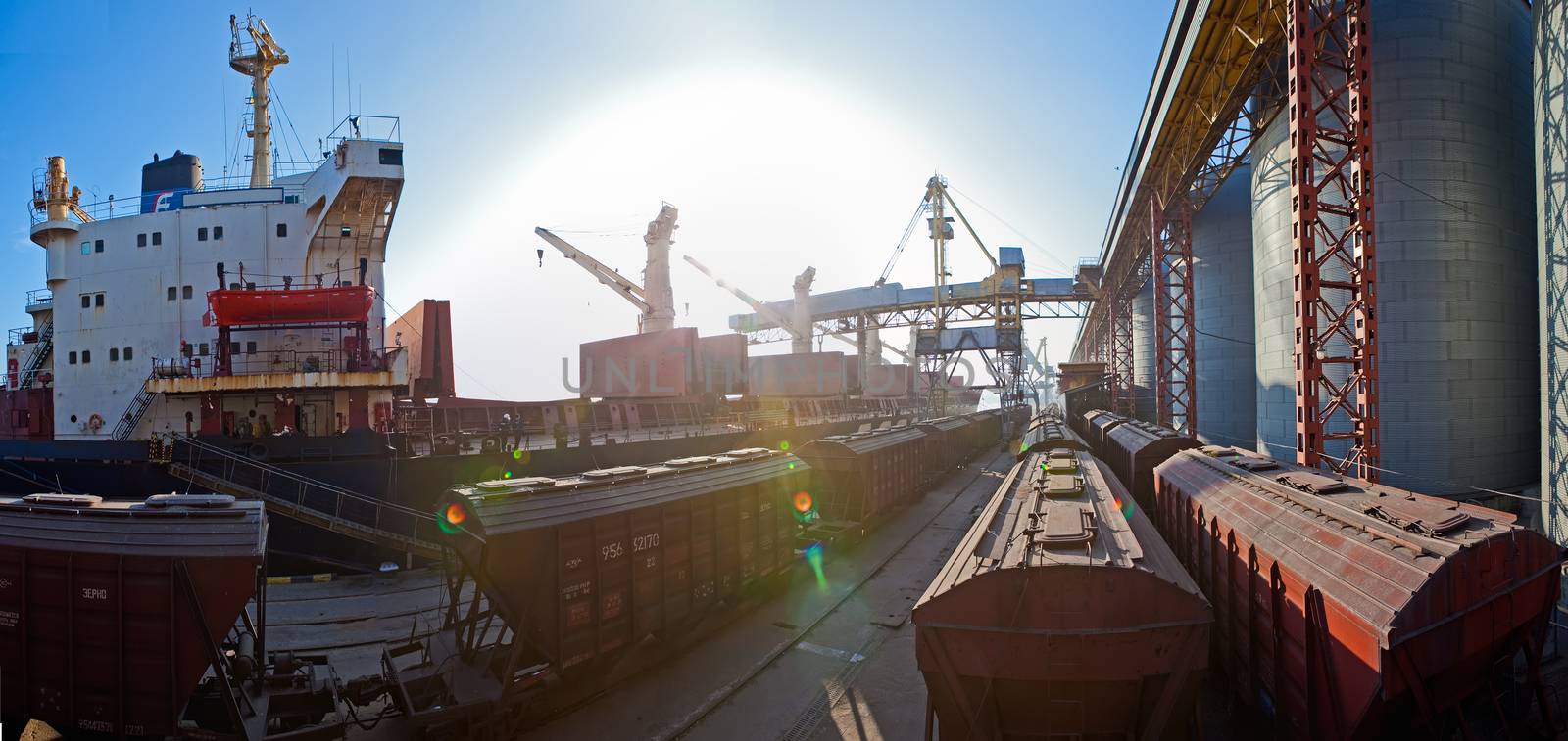 Grain from silos being loaded onto cargo ship on conveyor belt by sarymsakov