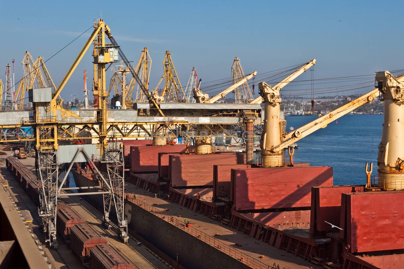 Grain from silos being loaded onto cargo ship on conveyor belt by sarymsakov