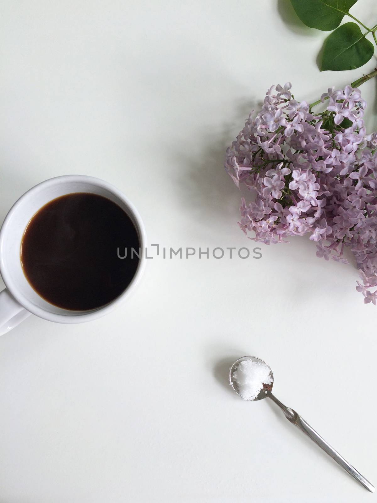 Black coffee in a cup, sugar on a spoon and fresh lilac flowers