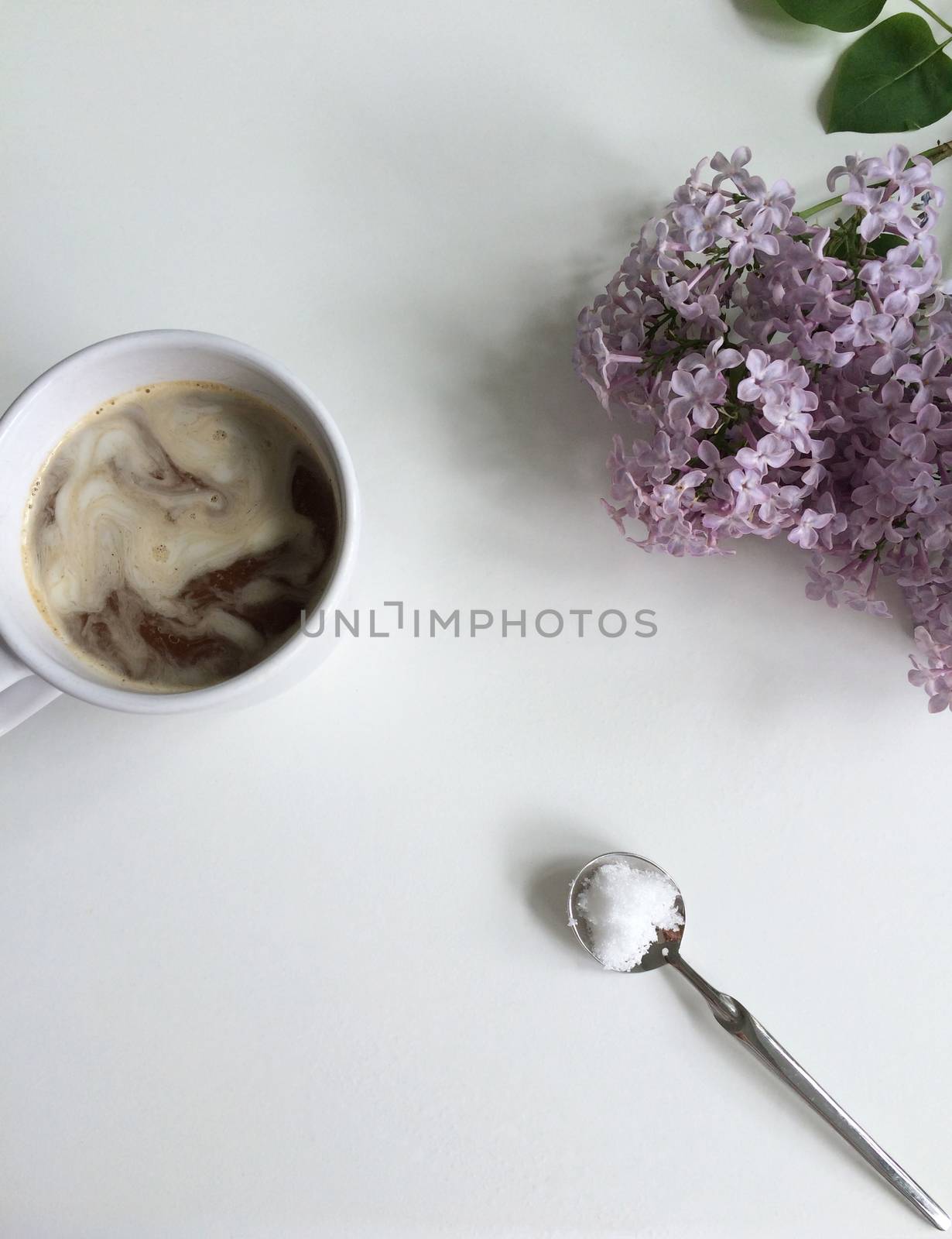 Coffee in a cup, sugar on a spoon and fresh lilac flowers