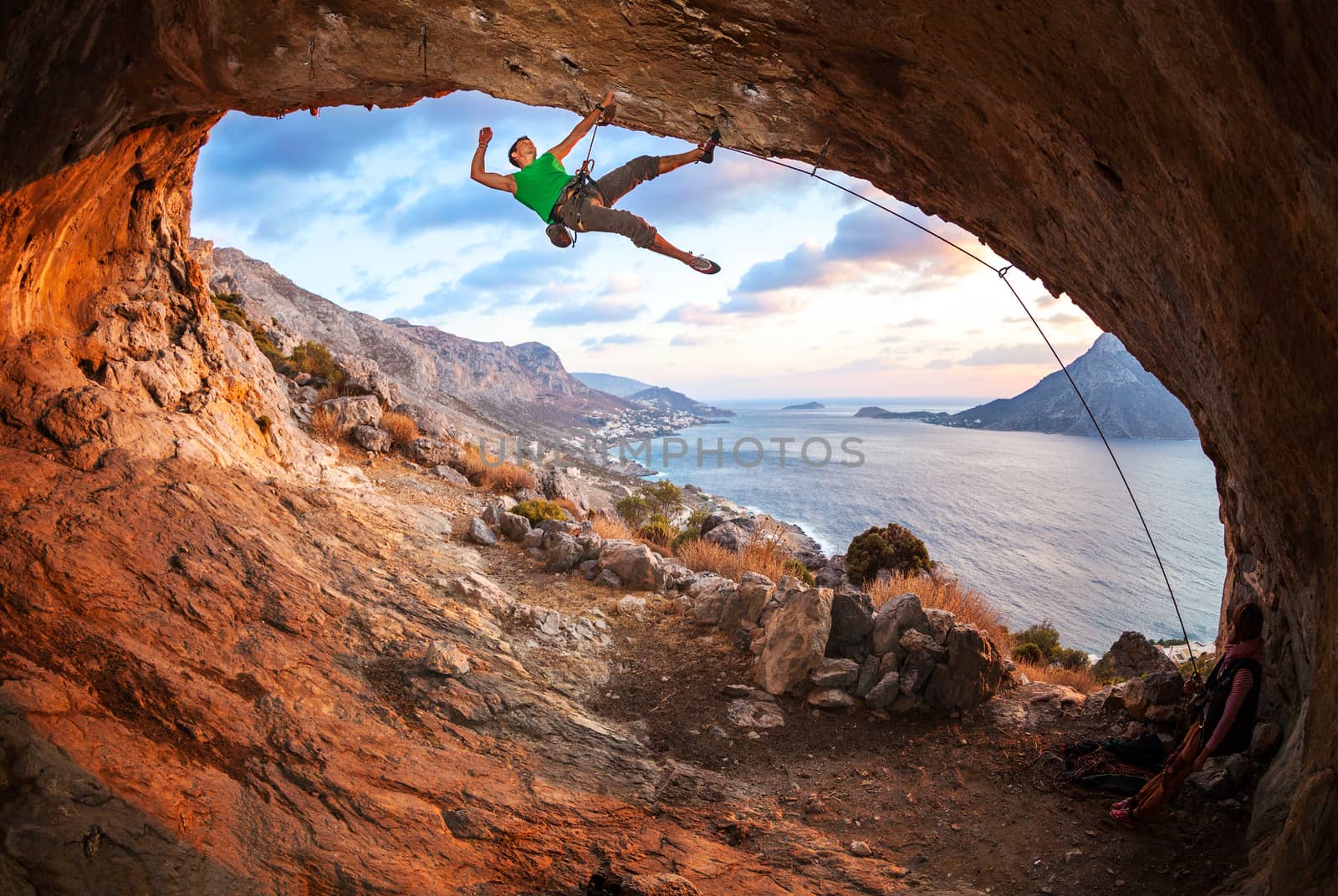 Male rock climber climbing along a roof in a cave by photobac