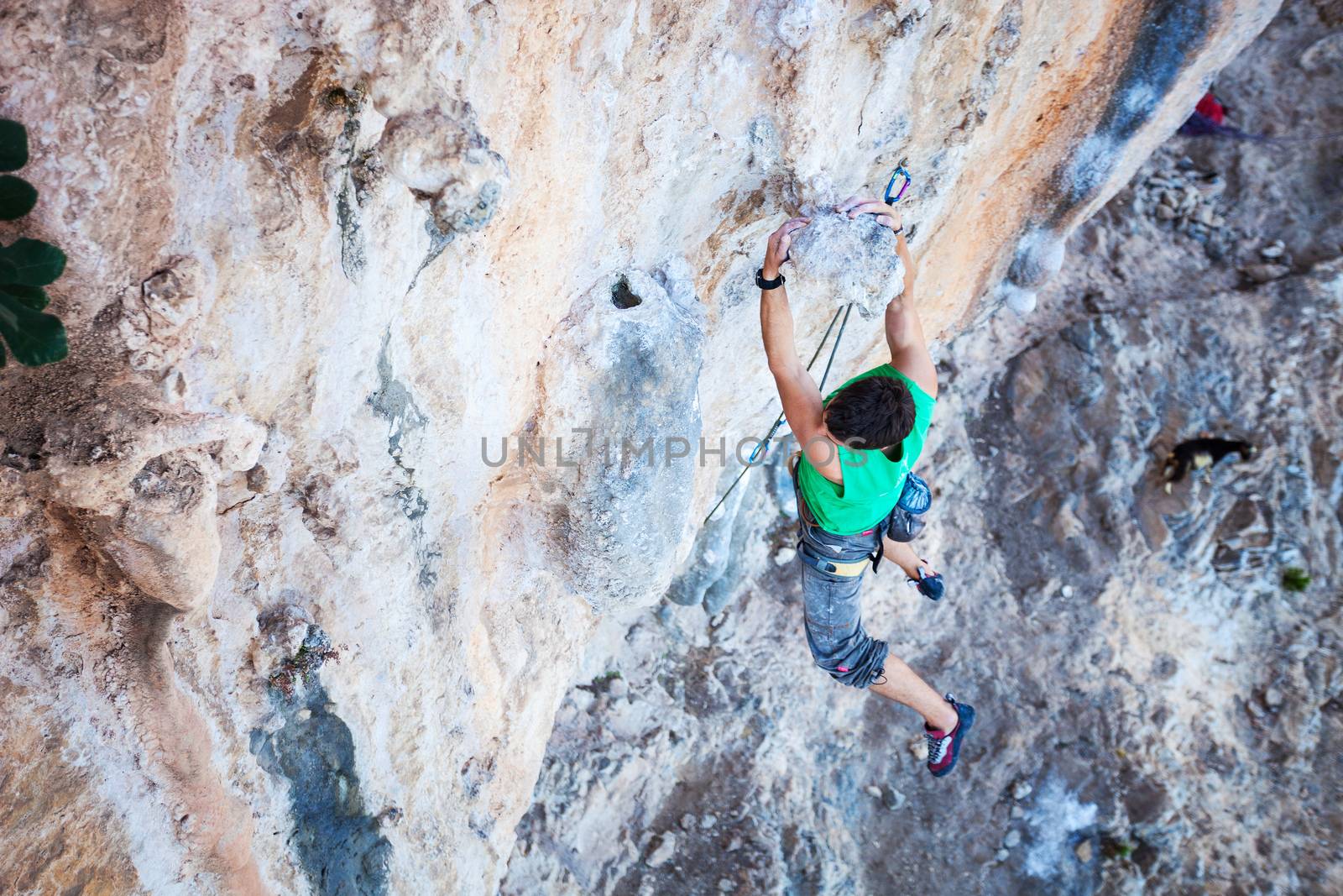 Climber holding on handhold while climbing cliff by photobac