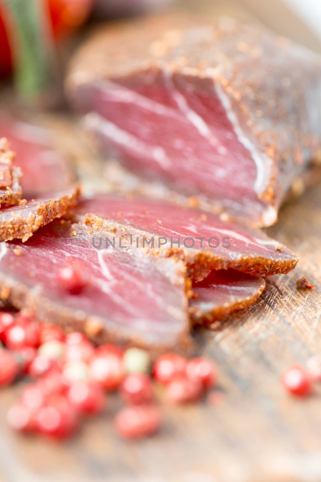 Prosciutto slices, pepper corn and tomatoes on wooden table