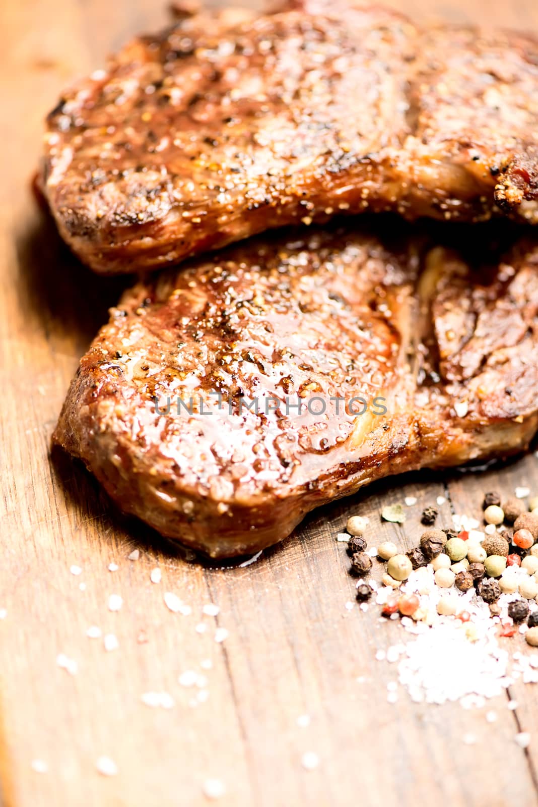 Succulent thick juicy portions of grilled steaks on an old wooden board with salt and pepper