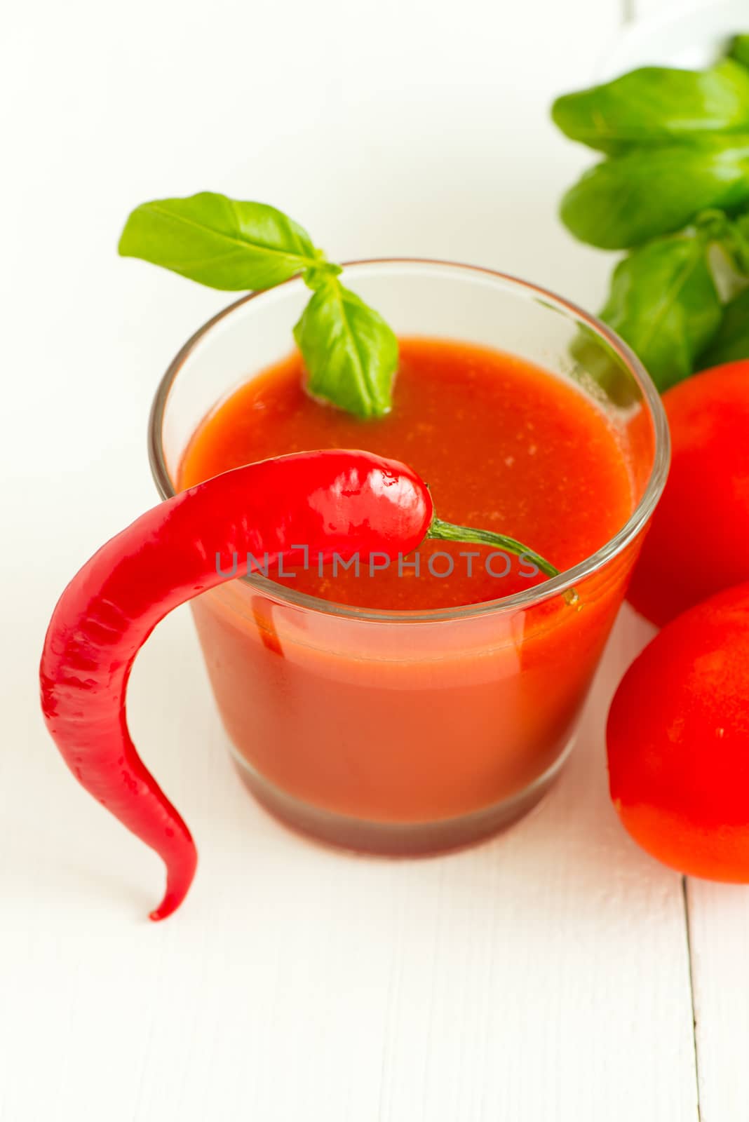Tomato juice, chili pepper and basil leaf on white wooden background