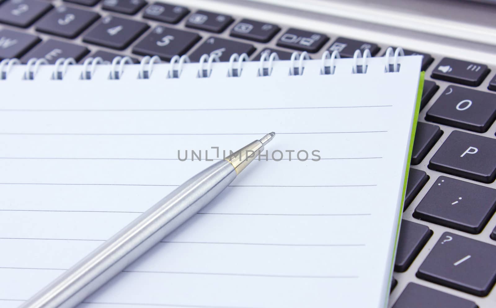 a notebook and pen lie on the keyboard of computer