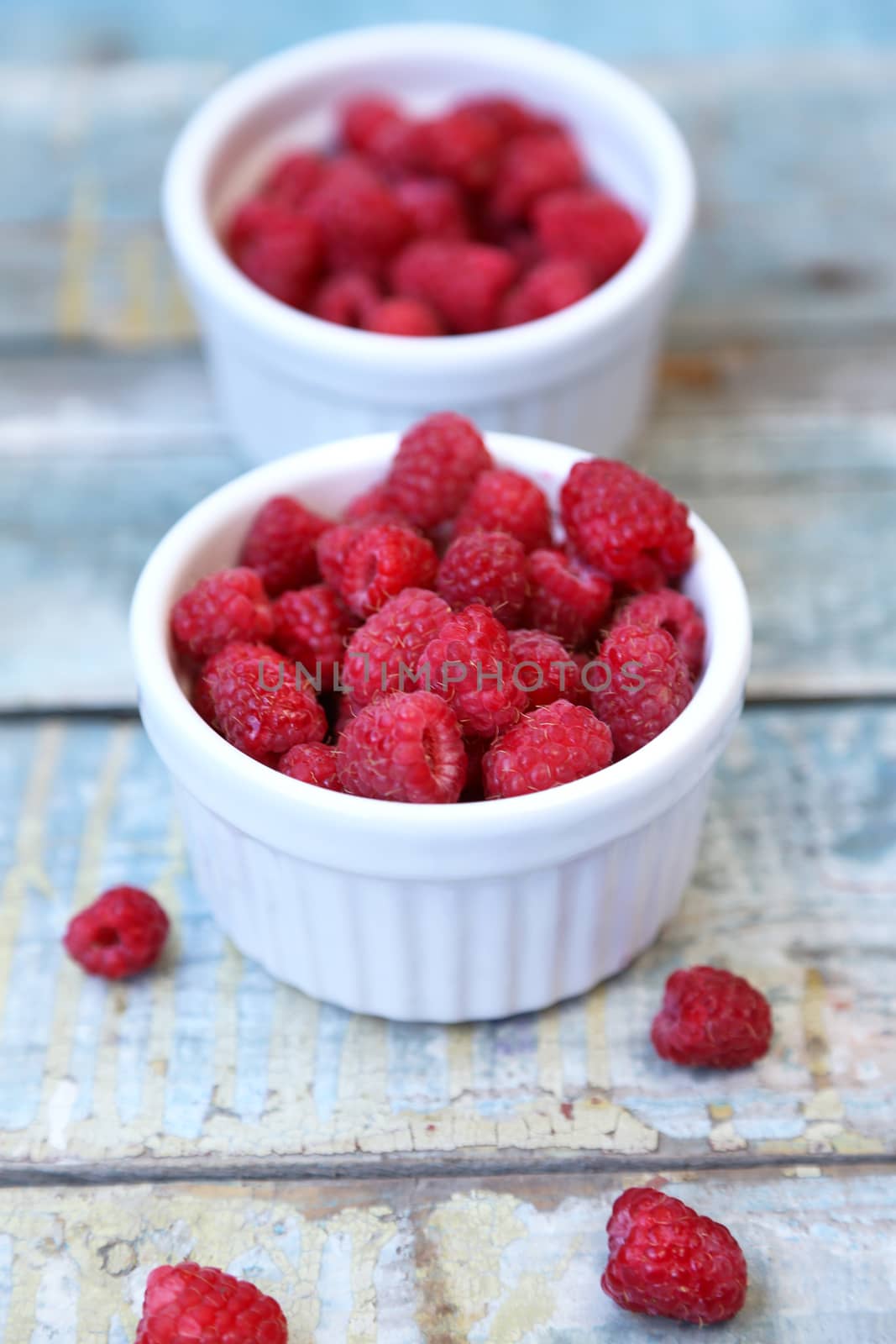 much fresh ripe raspberry in a white bowl on a wooden background
