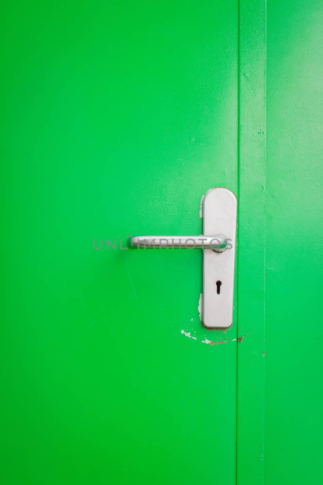 Metal door handle on green steel door, with keyhole