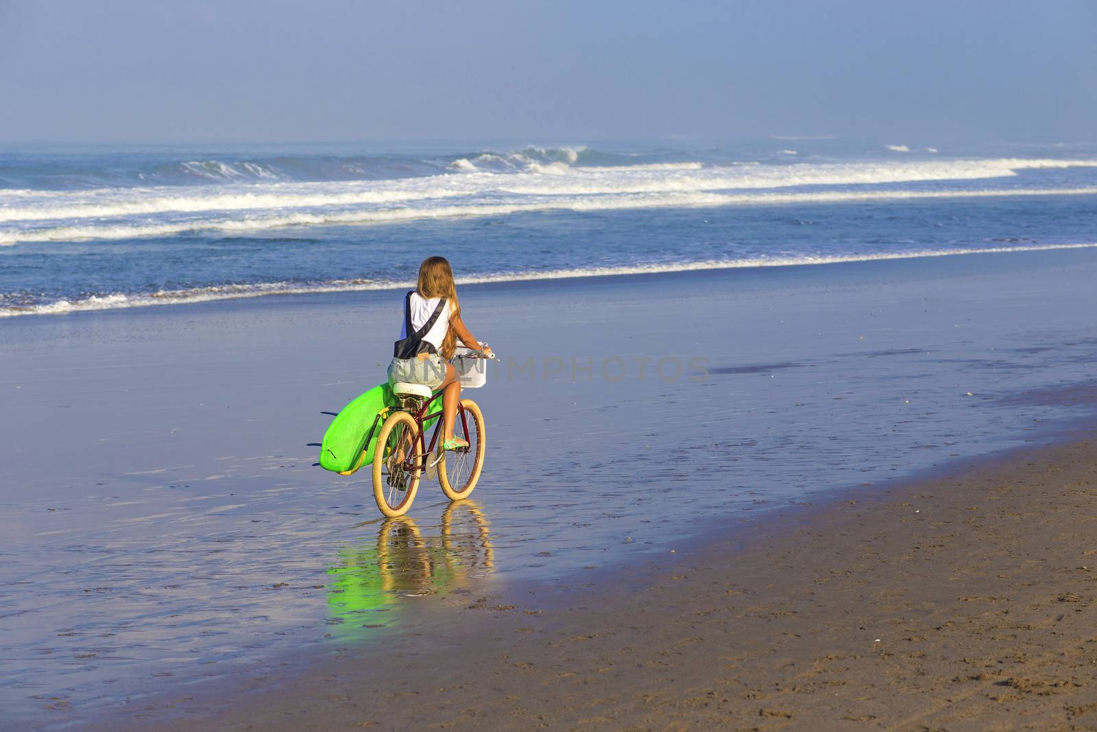 Young girl with surfboard and bicycle on the beach.