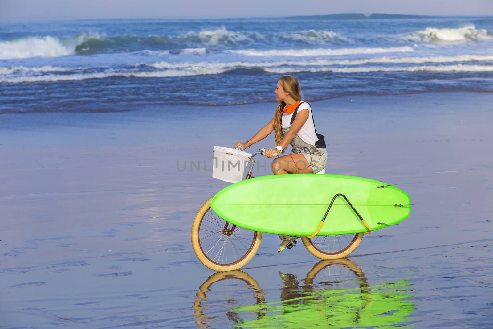 Young girl with surfboard and bicycle on the beach.