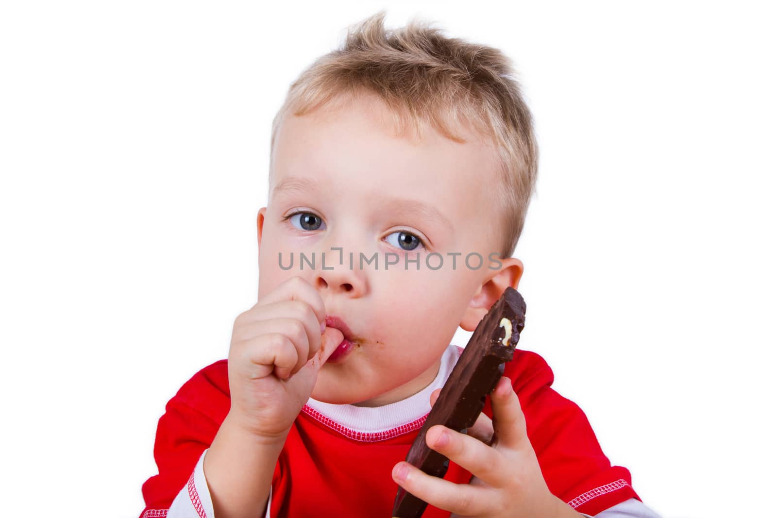 A small boy in red shirt eating whole bar of chocolate. Isolated on white background
