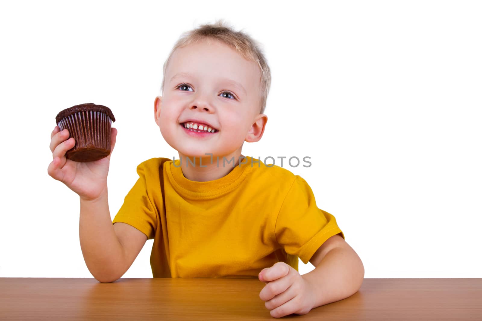 A small boy in yellow t-shirt eating a chocolate muffin. Isolated on white background