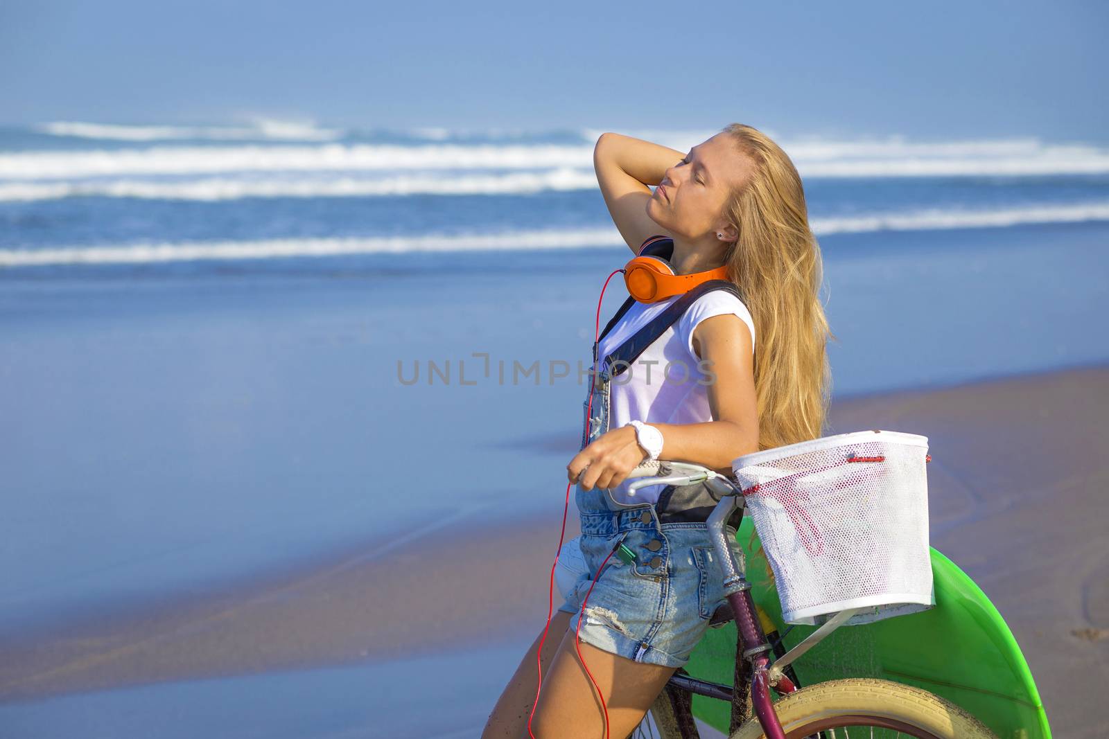 Young girl with surfboard and bicycle on the beach.