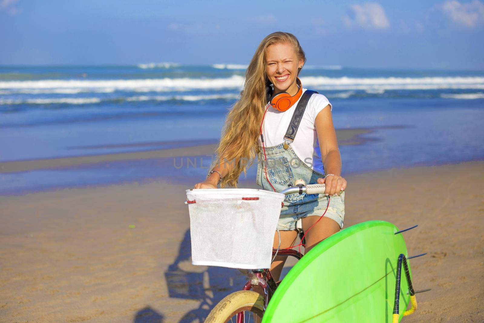 Young girl with surfboard and bicycle on the beach.