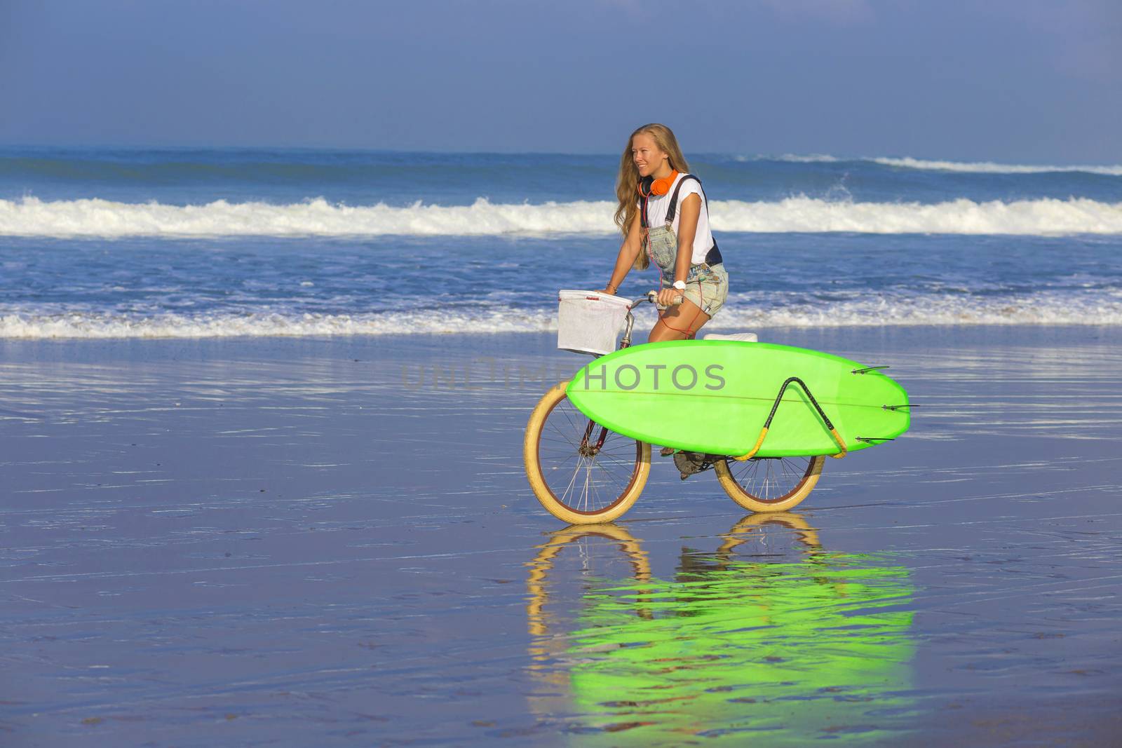 Young girl with surfboard and bicycle on the beach.