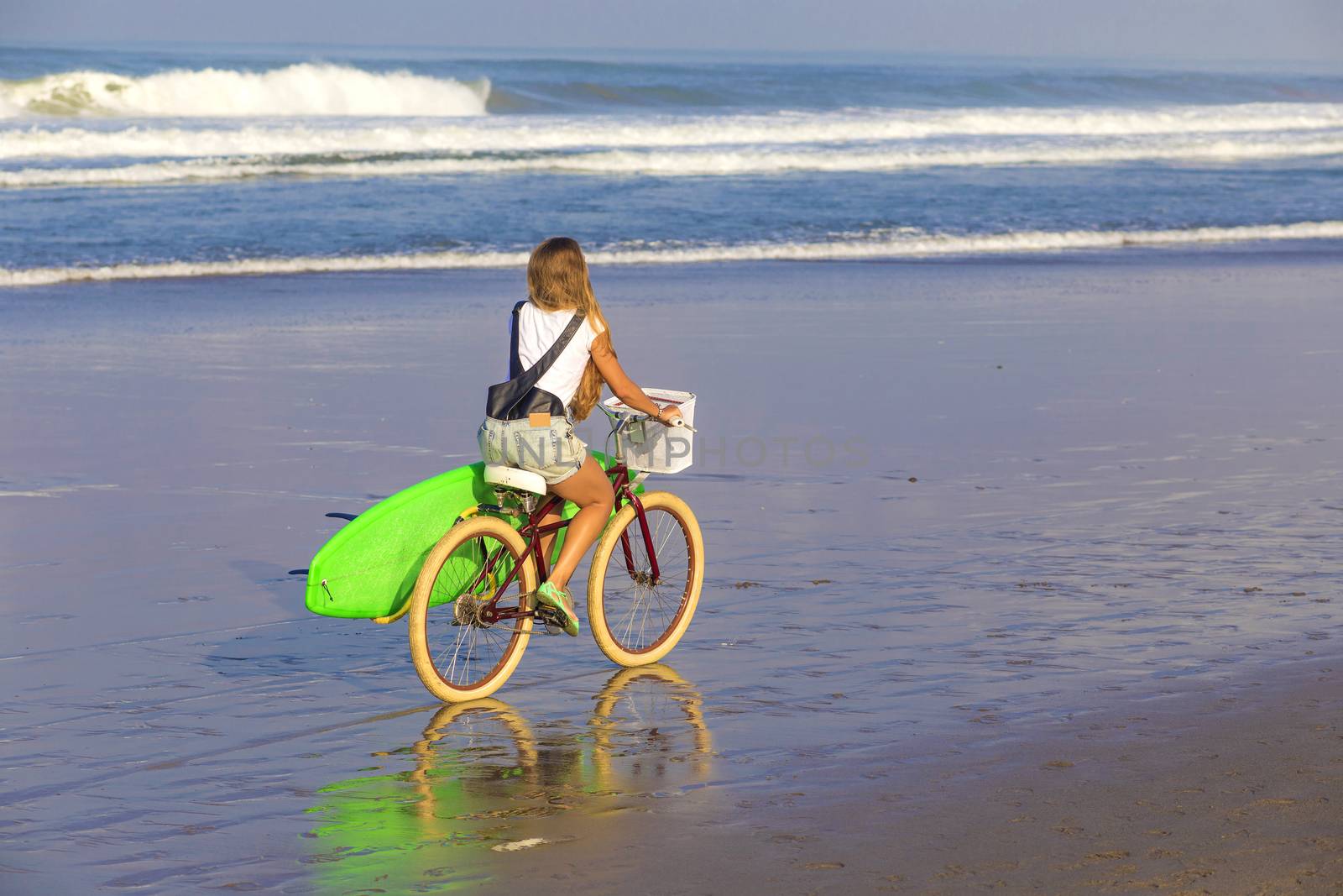 Young girl with surfboard and bicycle on the beach.