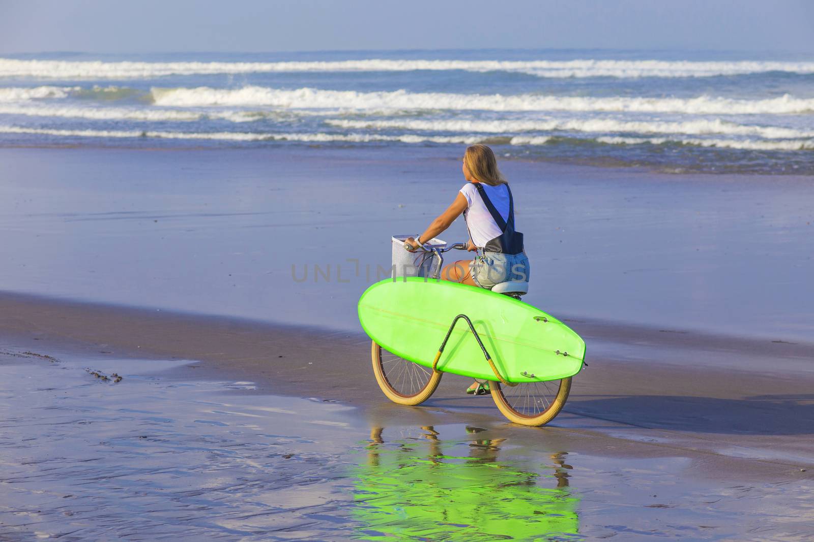 Young girl with surfboard and bicycle on the beach.